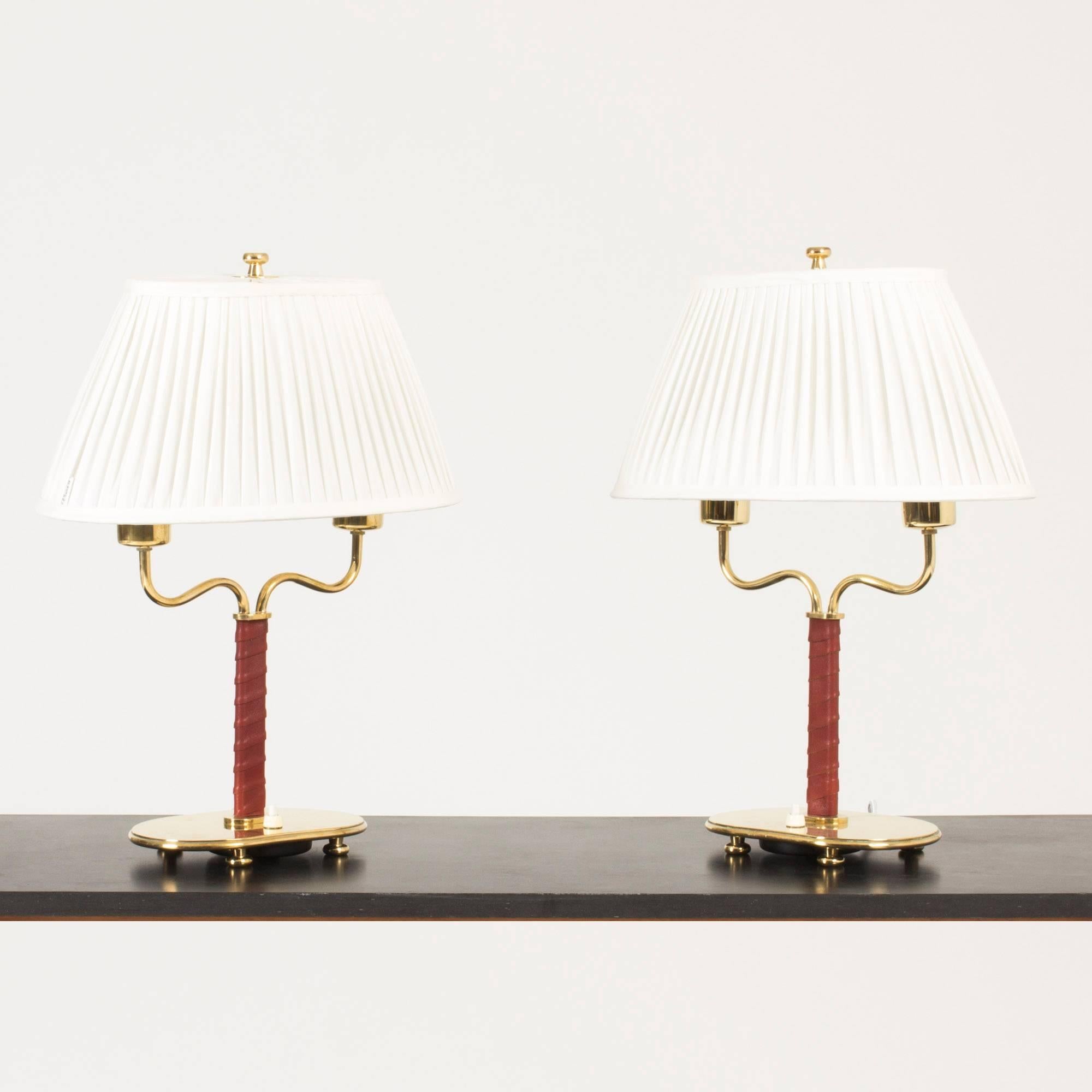 Pair of beautiful, exceptionally elegant table lamps by Josef Frank. Made from brass with little feet under the bases, handles wreathed with oxblood leather. Oval shaped white shades with brass knobs at the top.