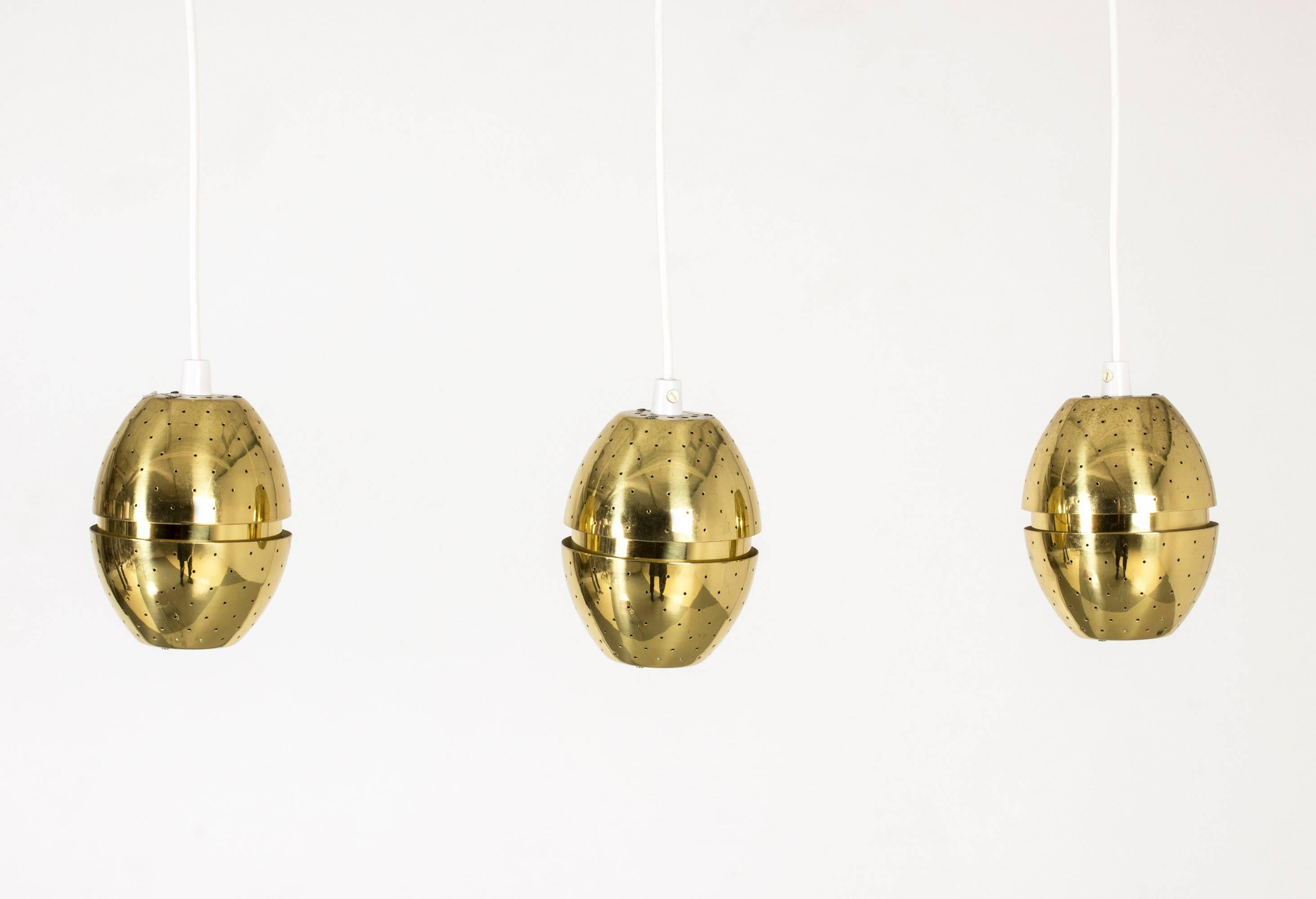 Set of three cool, egg-shaped brass pendant lights by Hans-Agne Jakobsson. The lights have separate wiring and are often used as window lights. Beautiful when lit with little points of light coming from every hole.