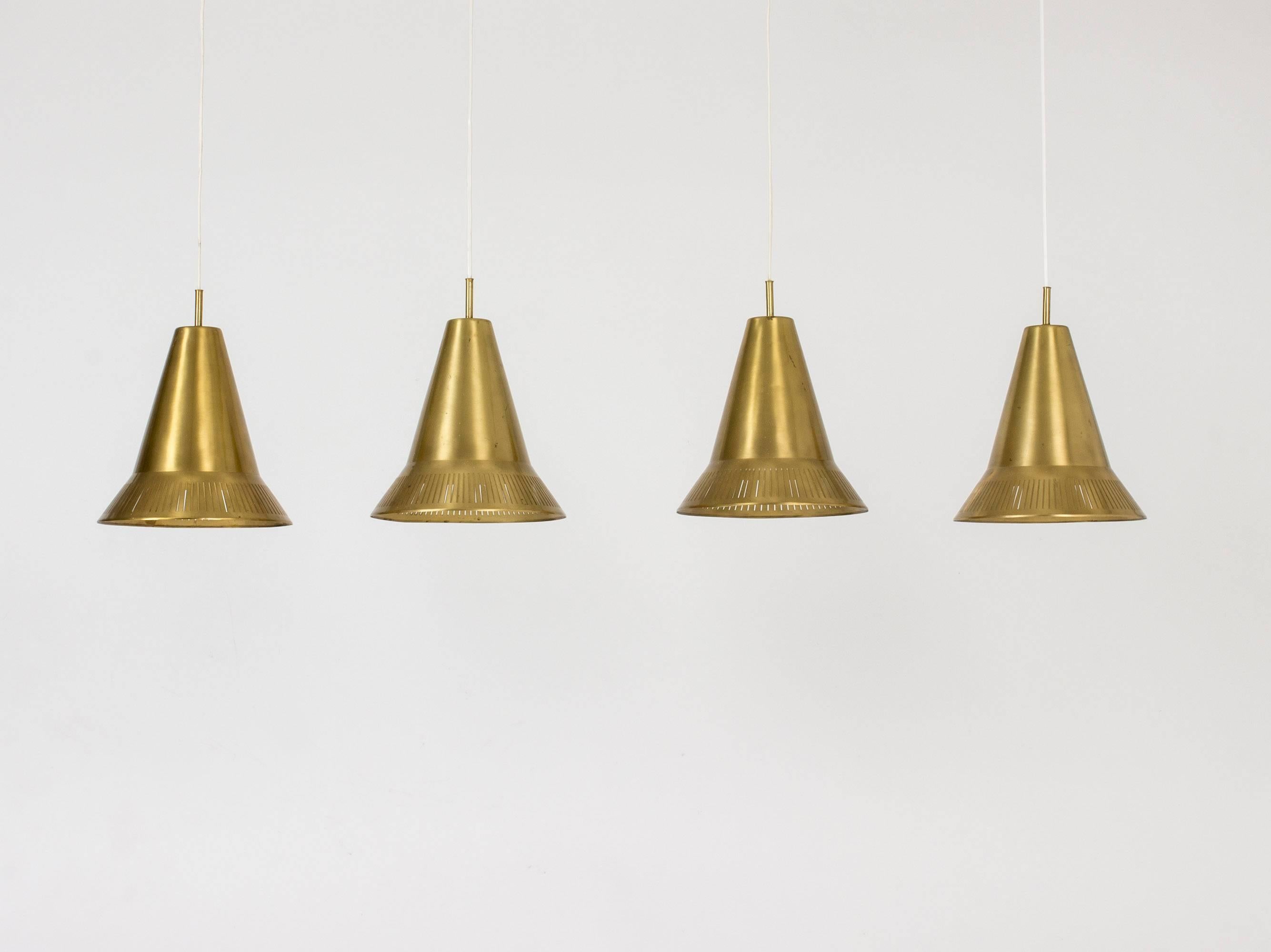 Set of four brass pendant lamps by Hans Bergström in a hat-like cone shape with perforated stripes around the base.