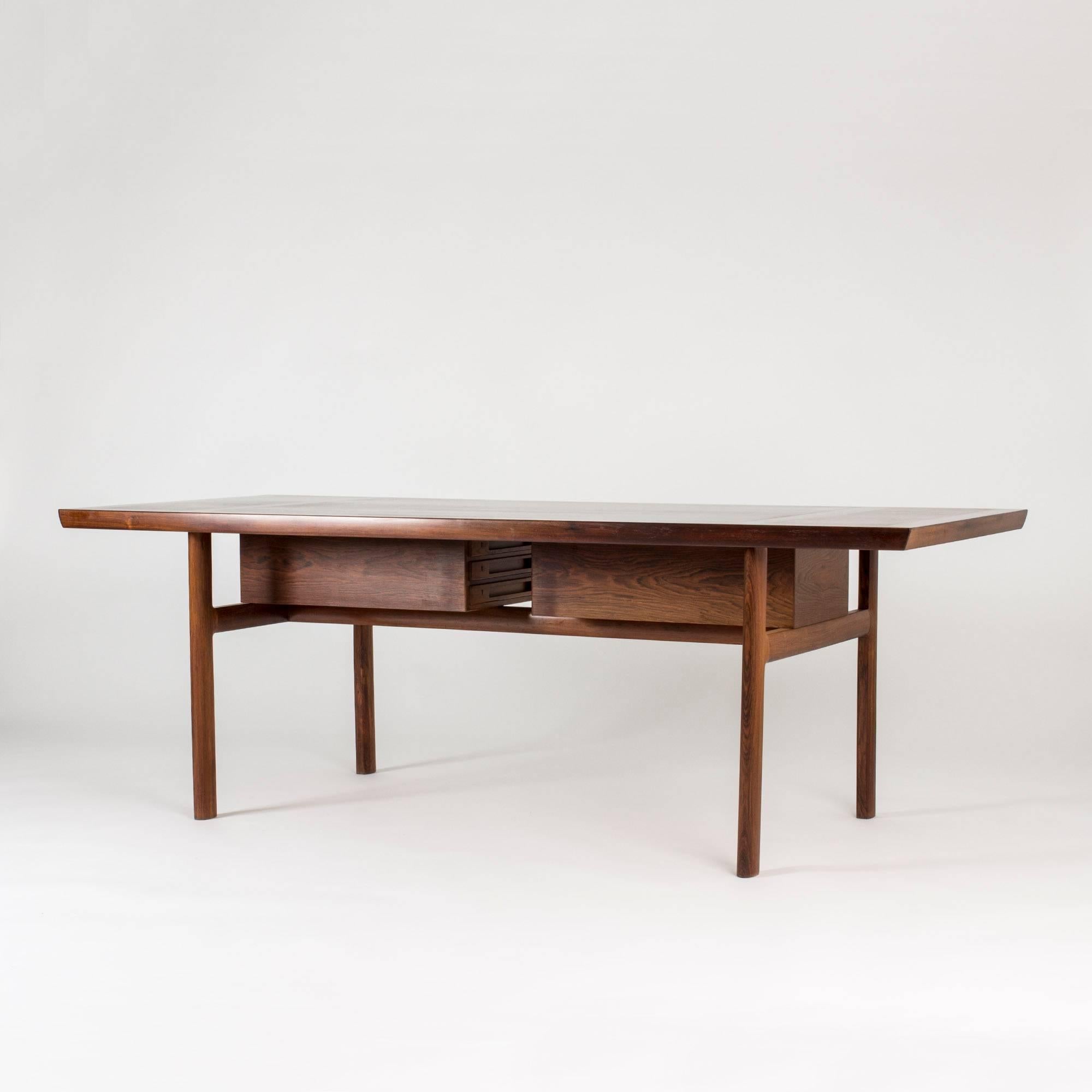 Imposing rosewood desk by Peter Hvidt & Orla Mølgaard. Hefty design with a thick table top and stout legs, contrasted with carefully carved drawer fronts. The drawers can be turned 90 degrees to face each other under the table, which gives extra leg