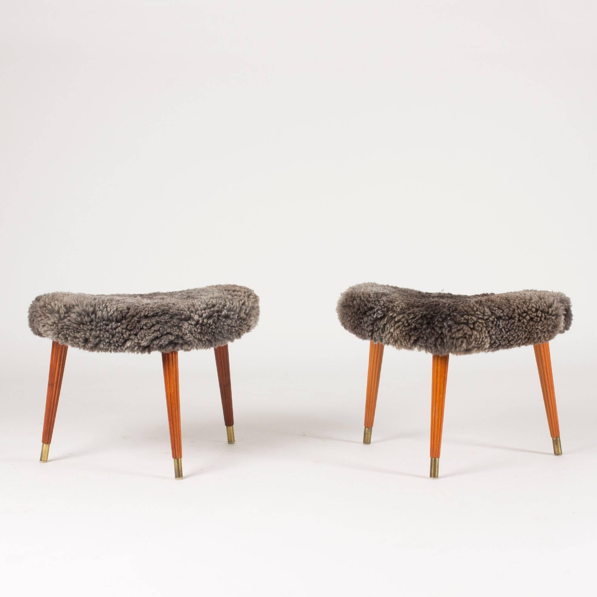 Pair of lovely kidney-shaped stools with seats dressed in sheepskin. Three mahogany legs on each stool with carved vertical striped and brass feet. Steady quality.