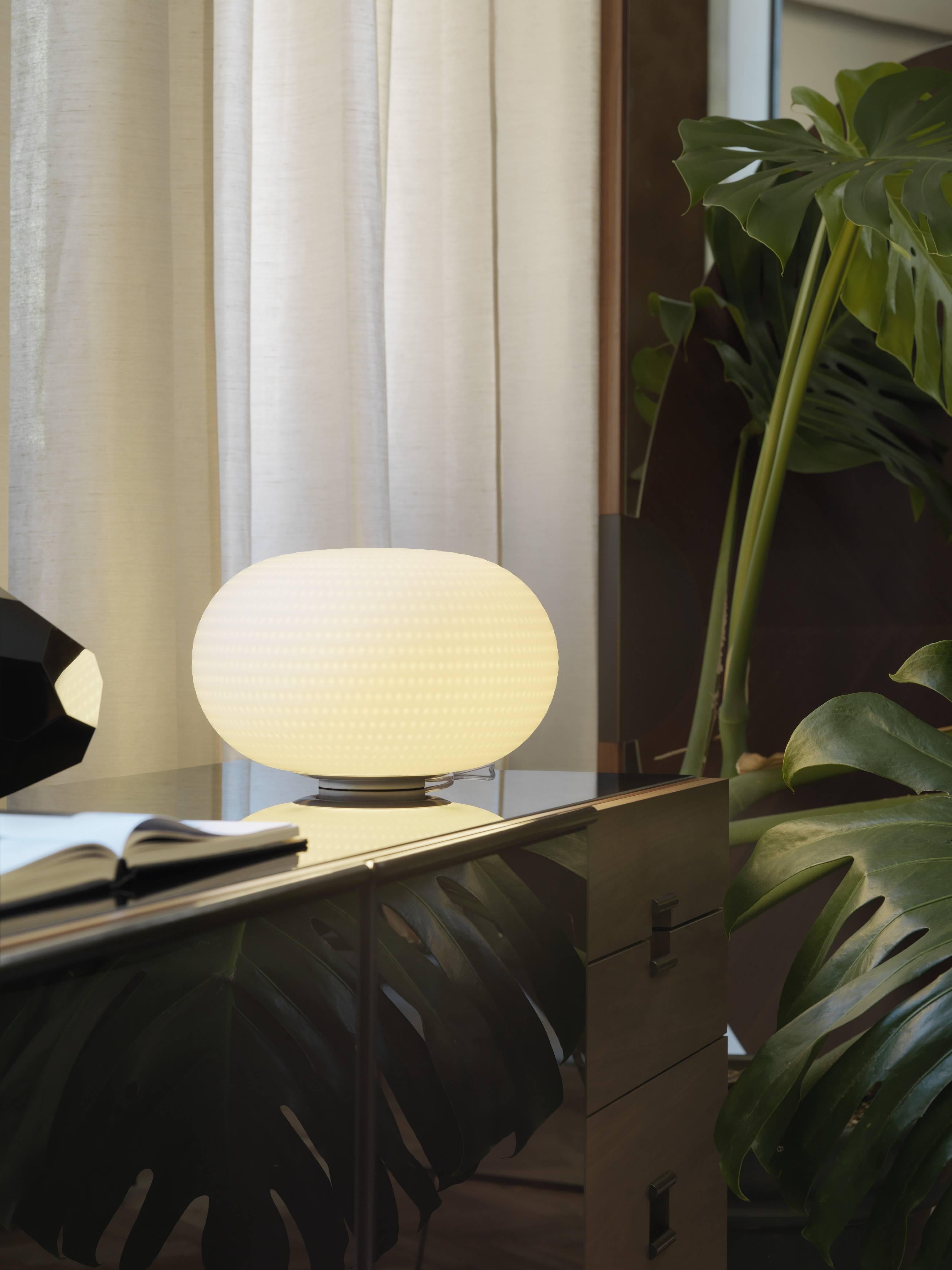 Lampada da tavolo media Bianca senza stelo di Matti Klenell da Fontana Arte.

La sua forma splendidamente equilibrata è arricchita e resa unica da una serie ordinata di delicate e leggere scanalature che, sul volume bianco del vetro, sembrano