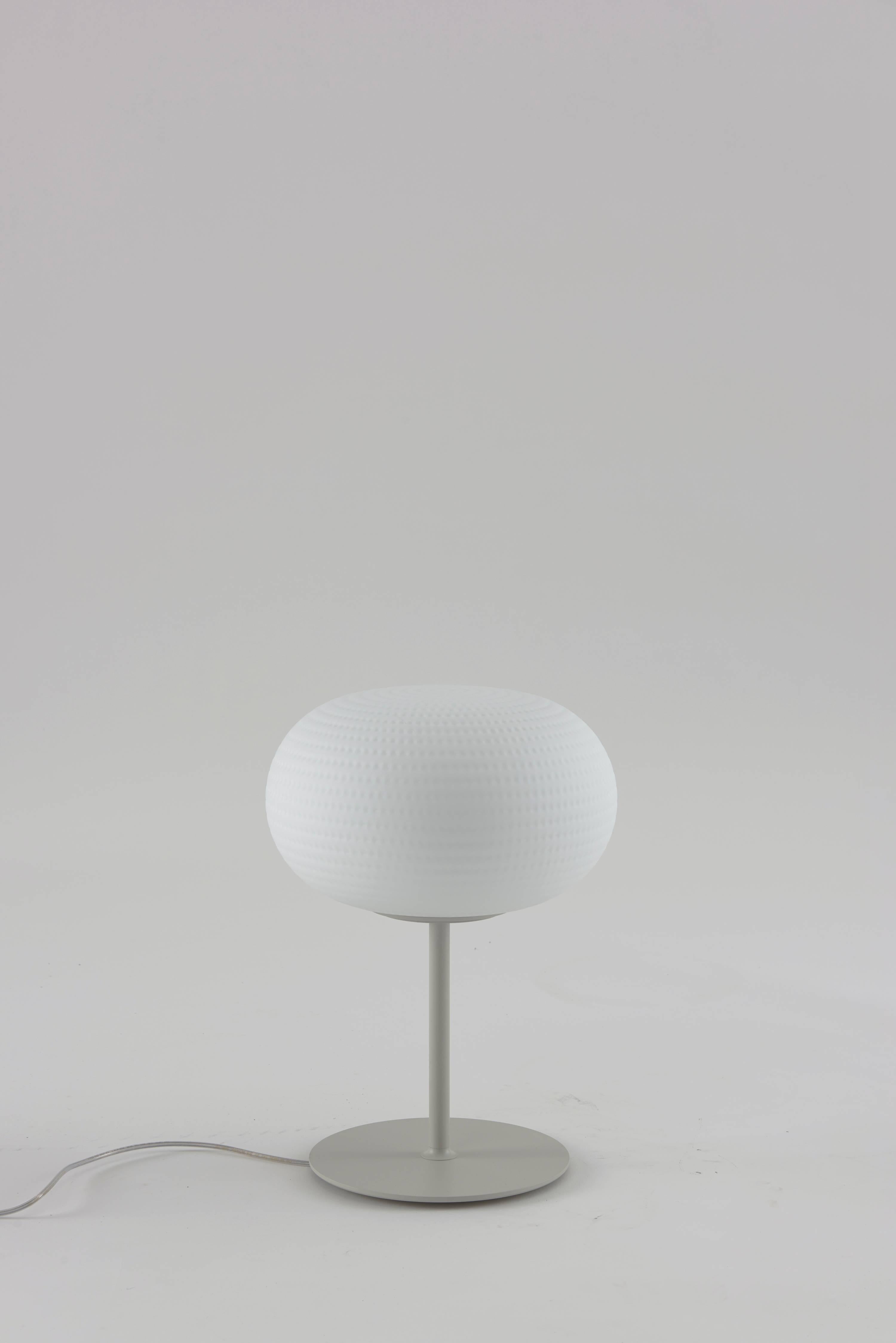 Bianca large table lamp with stem by Matti Klenell from Fontana Arte.

Its beautifully balanced shape is enriched and made unique by an orderly series of delicate, light grooves that, on the white volume of the glass, look like tiny prints on