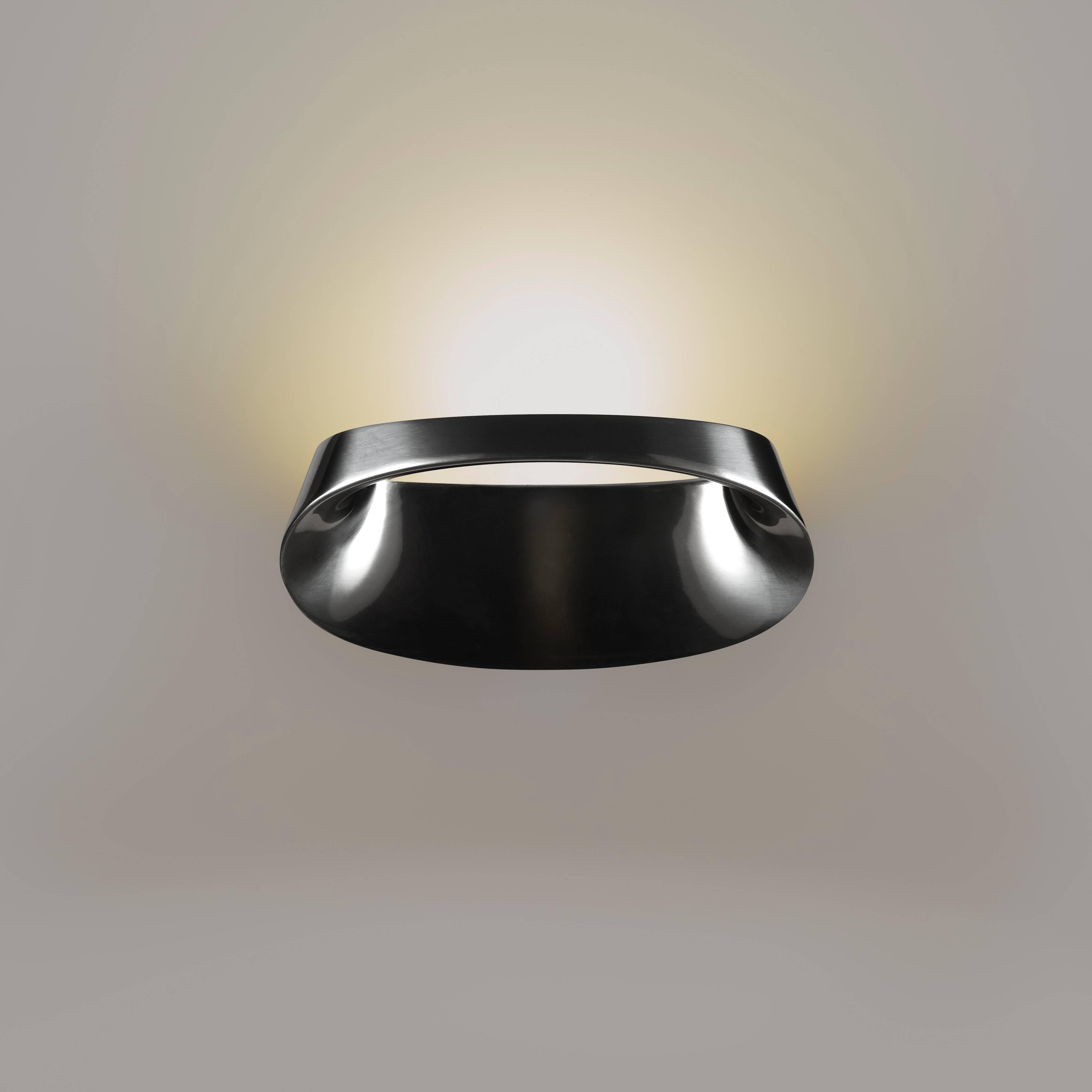 Manufactured in 2017 by Fontana Arte and designed by Odo Fioravanti in 2014, the Bonnet wall lamp in polished aluminum reworks the concept of indirect lighting. The top part conceals a small yet very powerful Led source whose ray of light is mainly