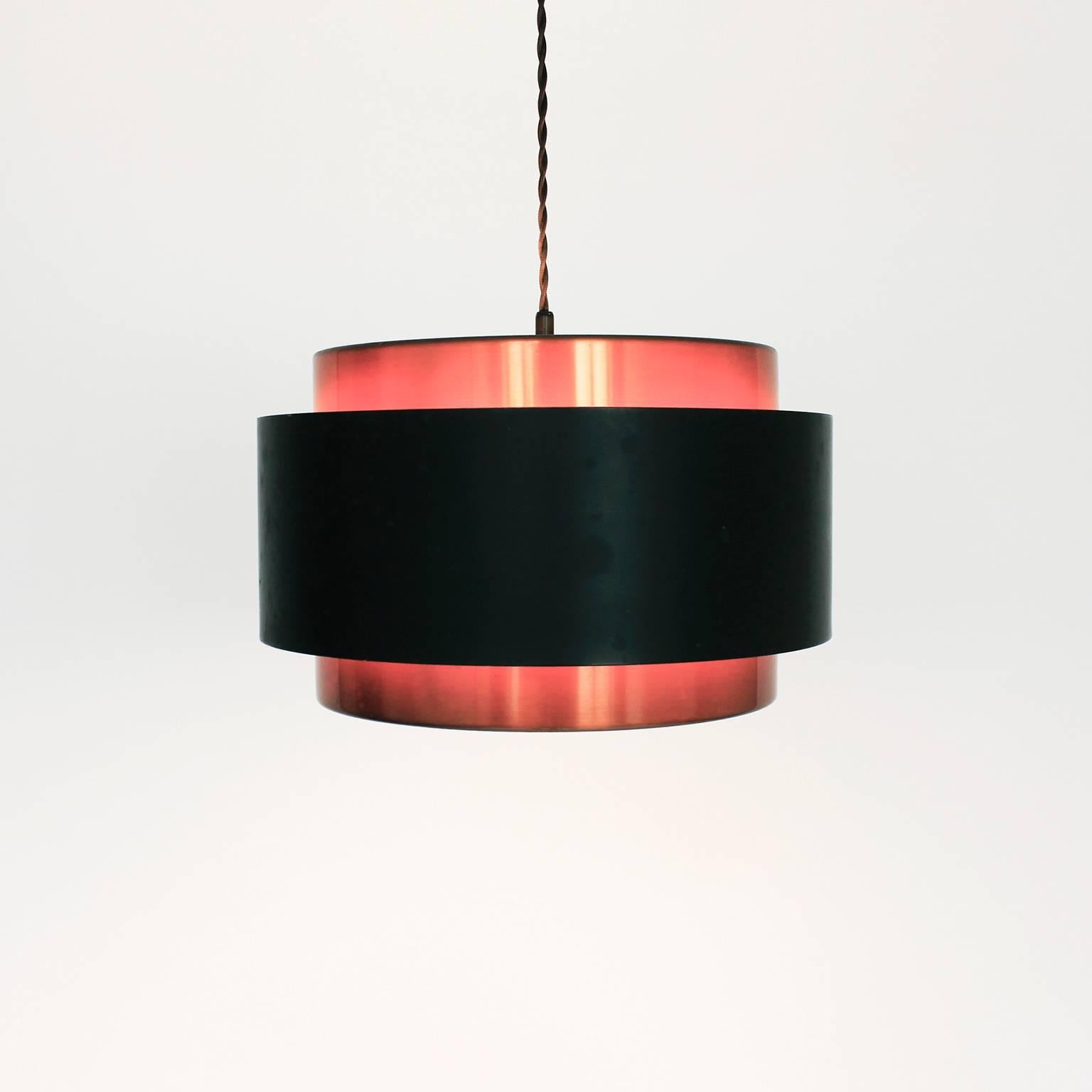 A simple yet beautiful Saturn suspension lamp in copper and black lacquered steel designed by Jo Hammerborg for Fog & Mørup. The lamp supports a single E27 bulb surrounded by two copper and one steel band (lacquered black on the outside and orange