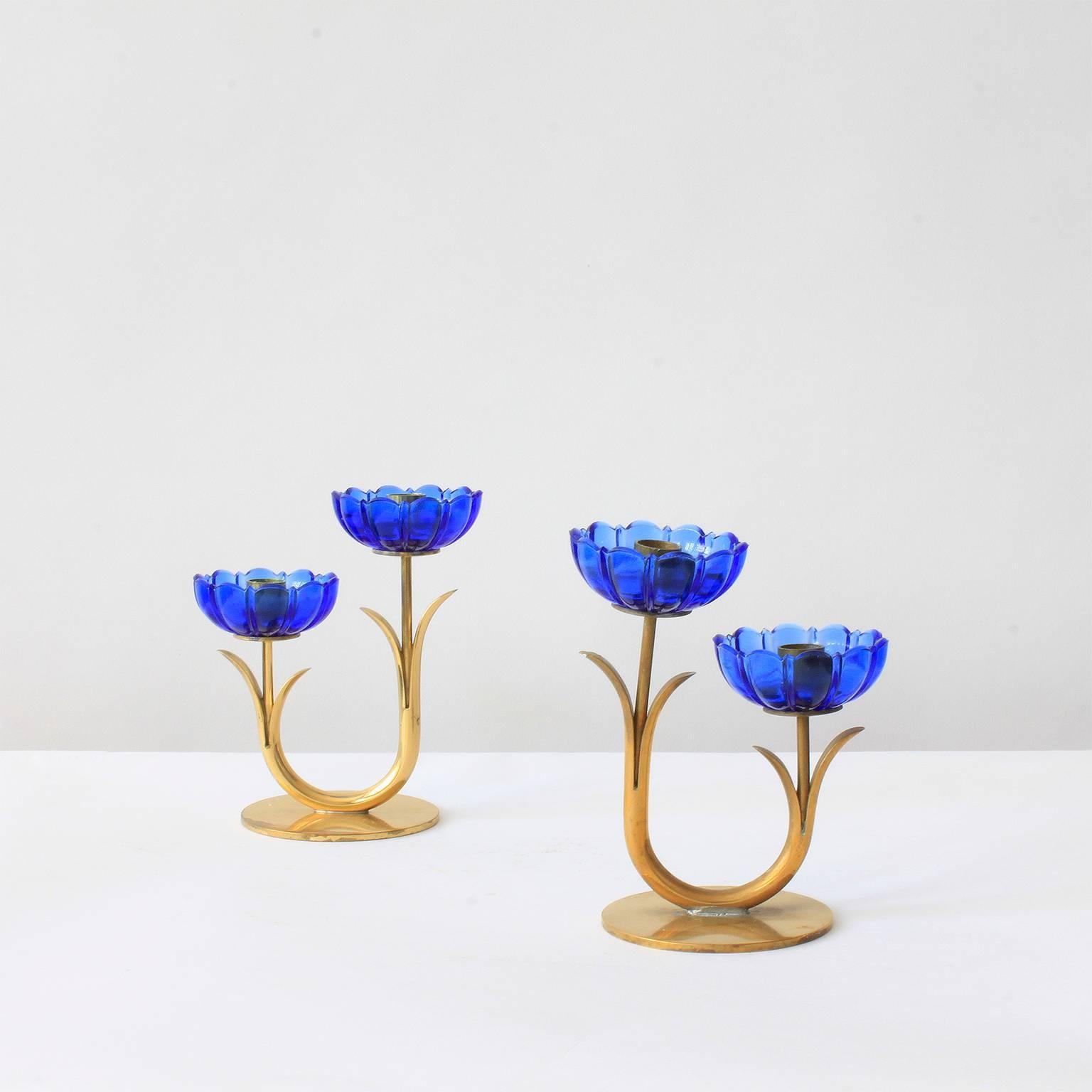 A set comprising three pairs of blue flower candleholders from Sweden. Designed by Gunnar Ander and marked by the manufacturer, Ystad Metall, on the base. These examples feature aged, patinated gold-plated brass stems. Each holder features two blue