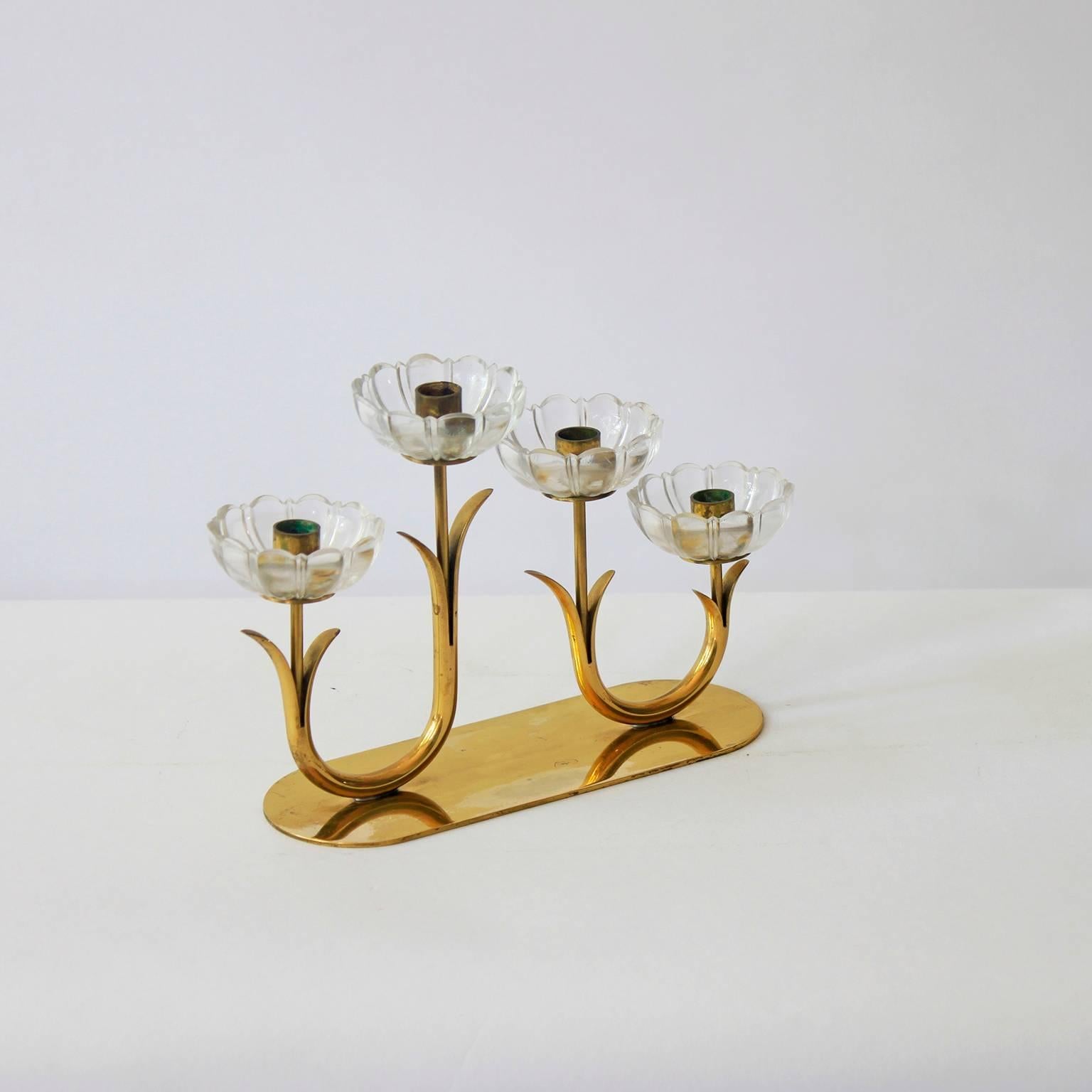 An elegant Swedish brass and glass flower candleholder comprising four clear glass flowers arranged on a brass platter. Designed by Gunnar Ander and marked by the manufacturer, Ystad Metall, on the base.