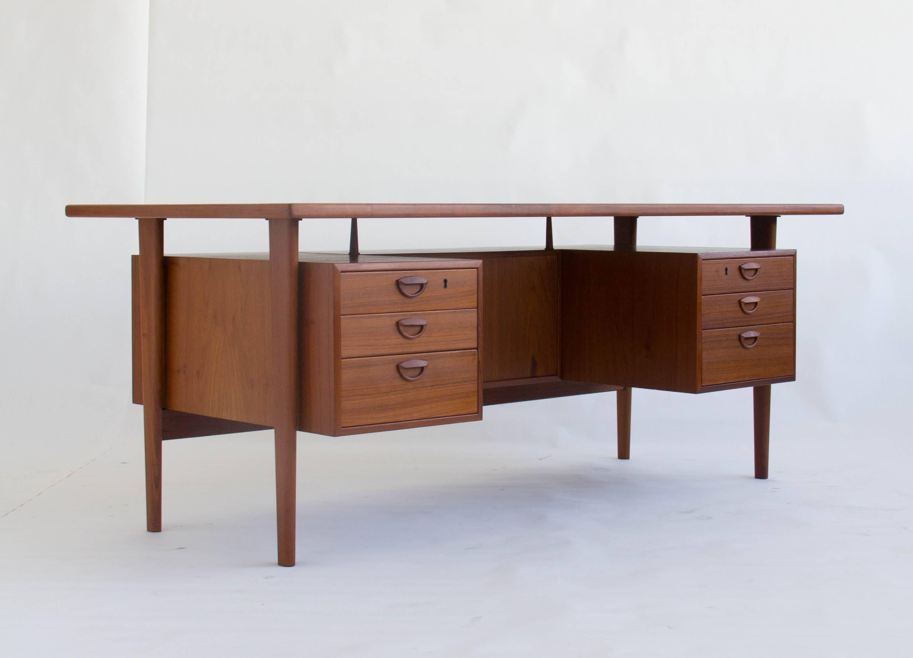 This striking floating teak desk by Kai Kristiansen features six drawers on the front side with handsome inset teak handles. On the back side of this desk there is one open section and two cabinet doors that contain storage compartments.