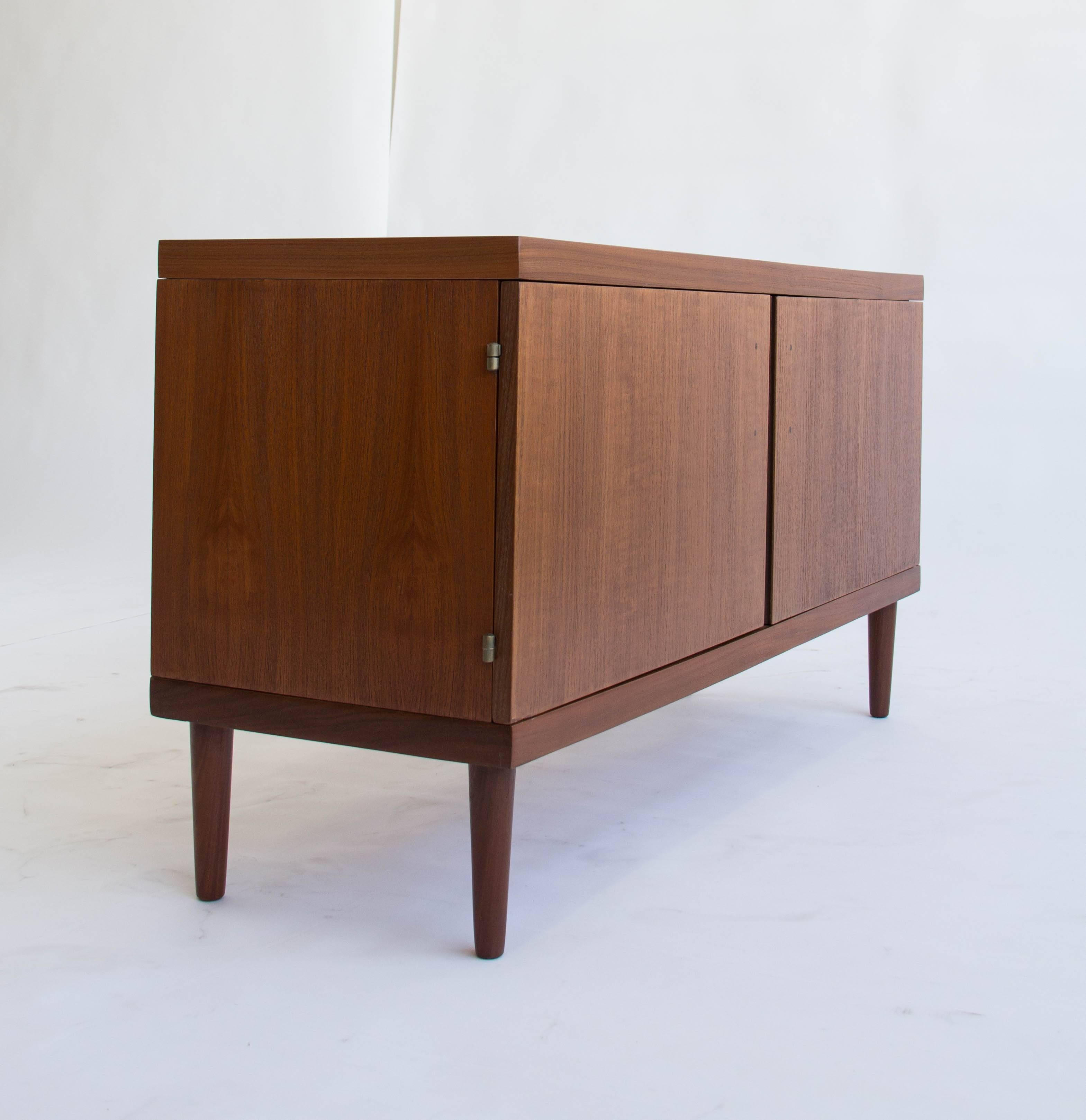 This a beautiful teak credenza in a Classic design by Hans Olsen. The modestly sized piece features two doors that swing open with sculpted door pulls. The interior is divided into two compartments, each with an adjustable shelf in beech wood.