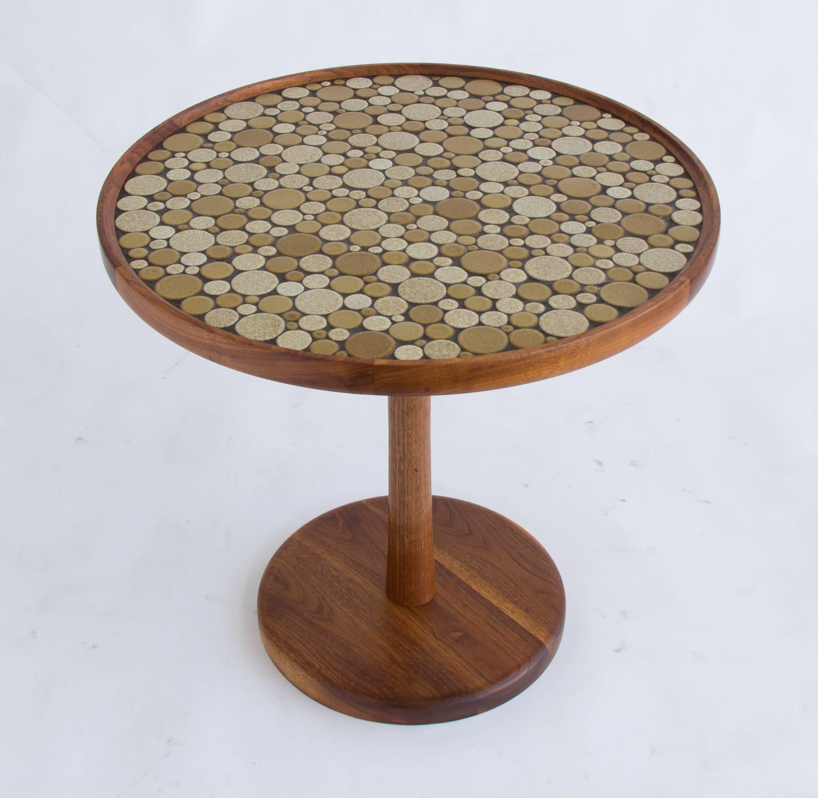 Round side table by Gordon & Jane Martz. The table top is inlaid with ceramic coin tiles in a neutral color palette. The frame, base and pedestal of the table are solid walnut. 

Condition: The table has been professionally cleaned and oiled and