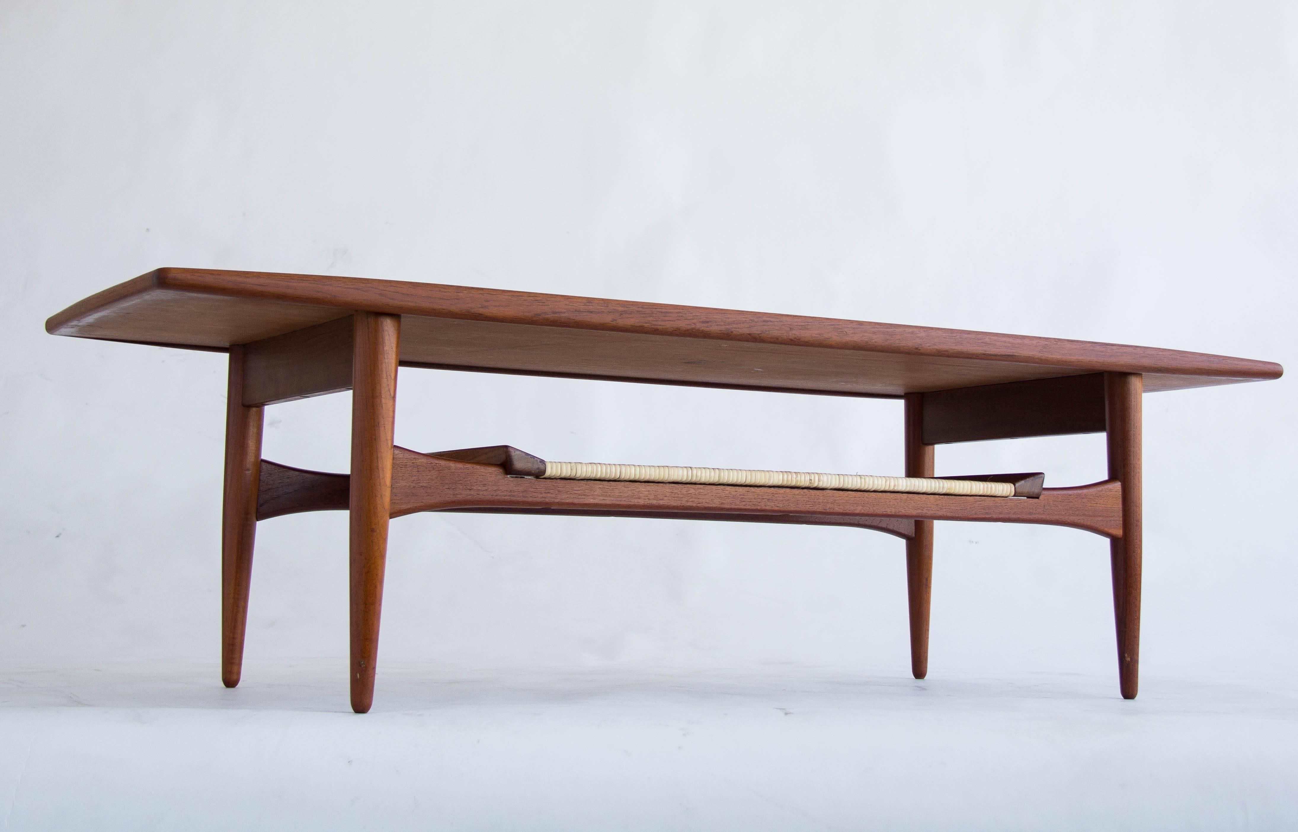Elegant surfboard-style coffee table manufactured for MM Moreddi of California in the 1960s. The tabletop is teak, with tapered legs, sculpted crossbars, and a woven cane shelf underneath.  

Condition: The table is in great vintage condition, and