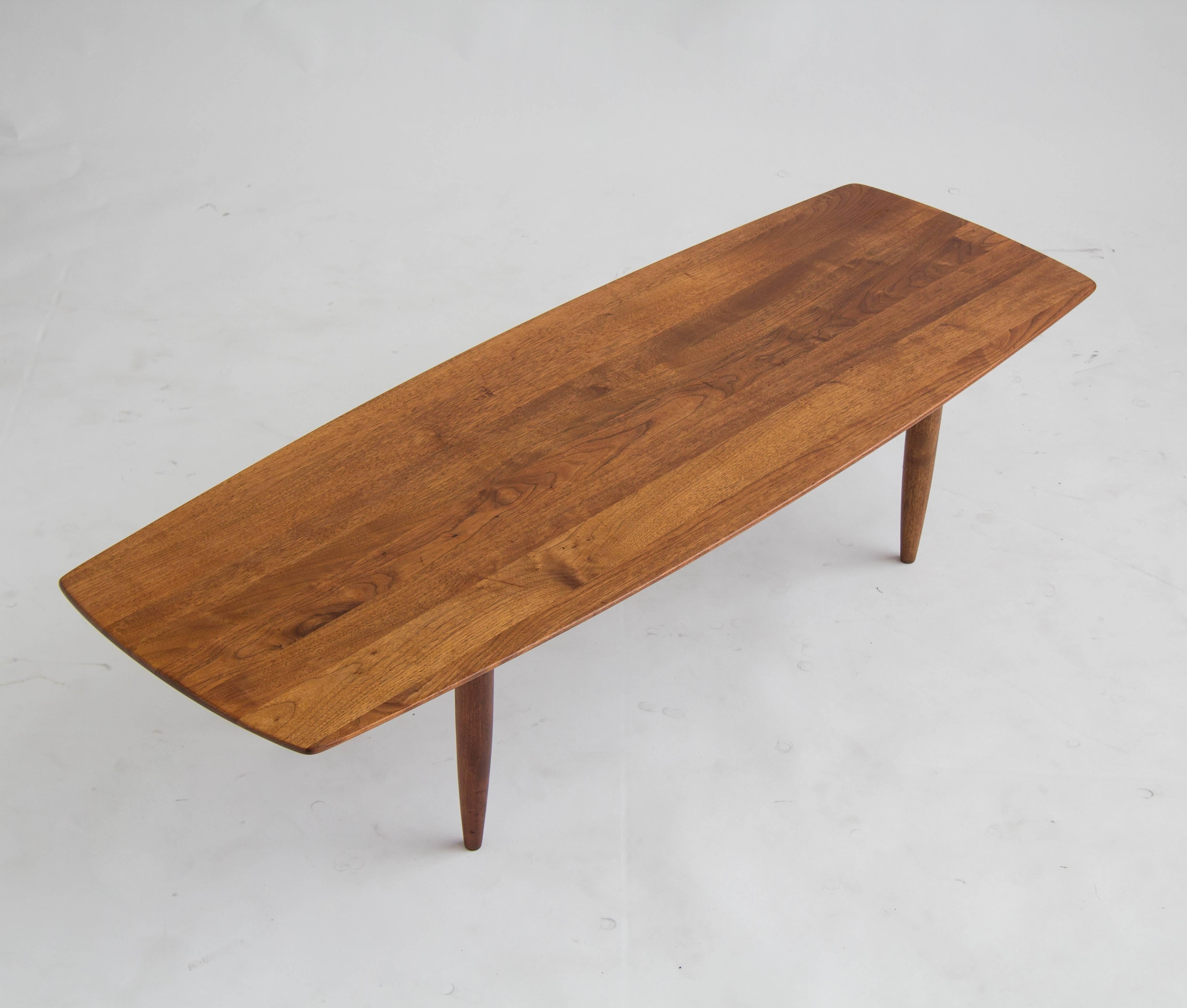 American-made solid walnut coffee table with a slightly rounded “surfboard” design. Tapered legs and rich walnut wood grain finish the look for a simple, elegant piece. 

Condition: Good vintage condition, with some minor signs of wear consistent