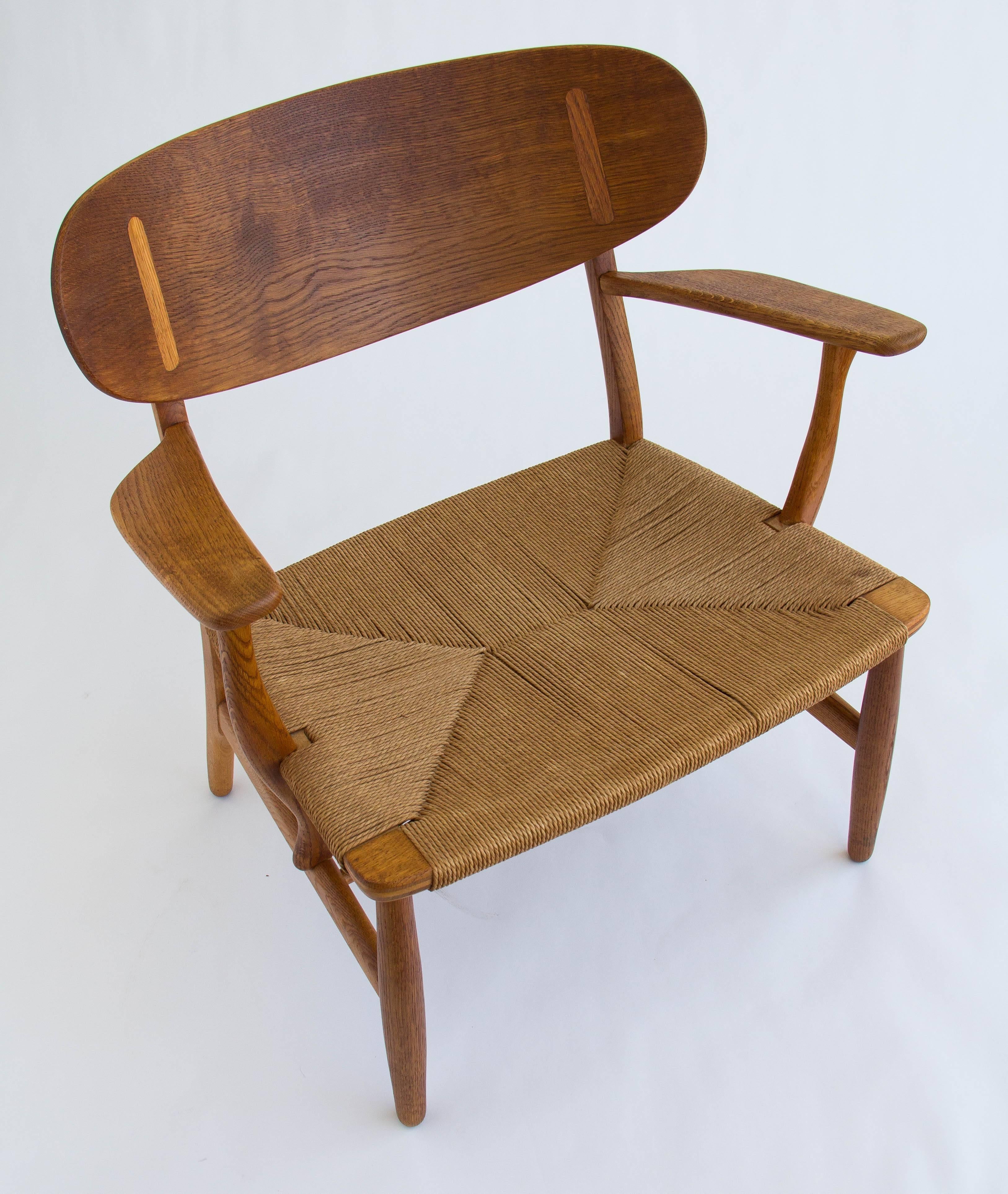 Wide armchair with oak frame and Danish paper cord seat. The design by Hans J. Wegner for manufacturer Carl Hansen & Søn features cantilevered armrests, inlay details on the curved backrest, and beautiful wood grain.

Condition: Excellent vintage