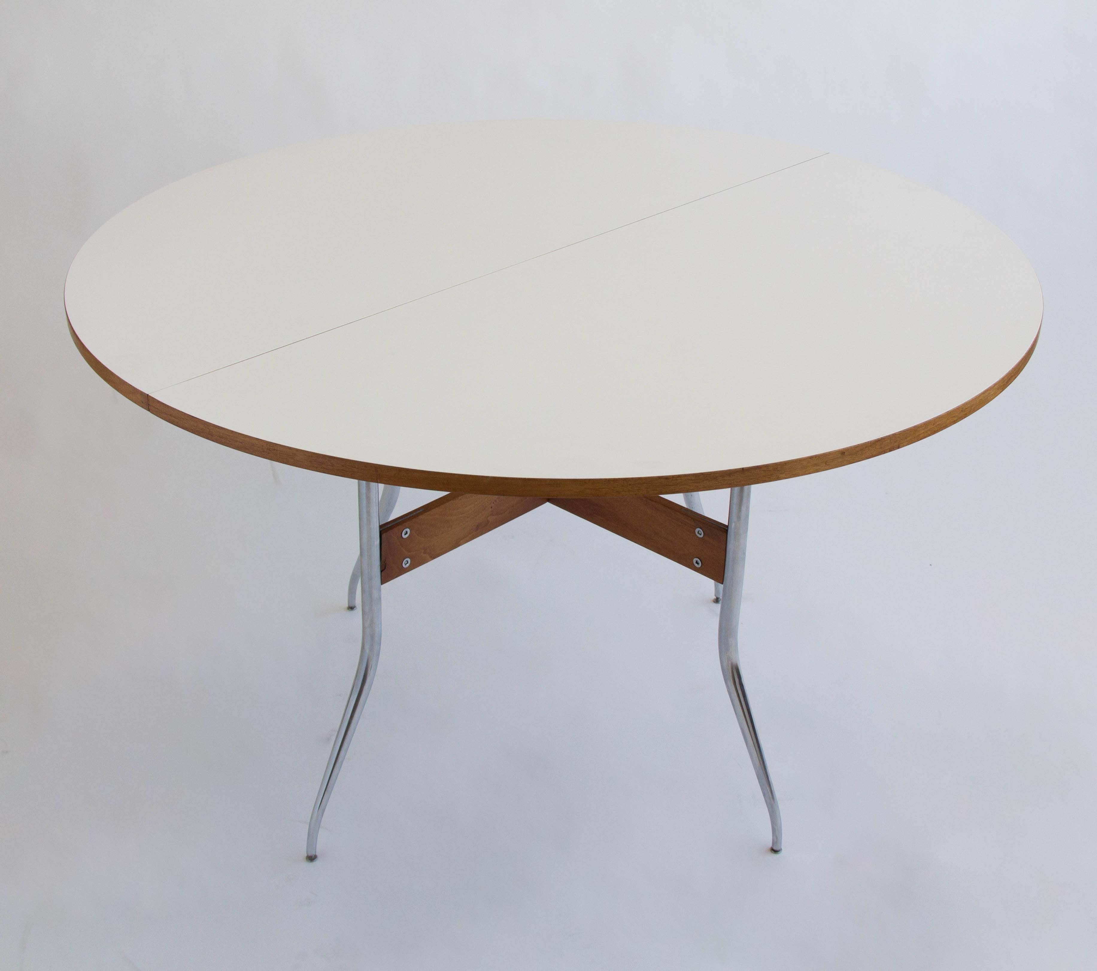 A round dining table from George Nelson’s coveted ‘Swag Leg’ group for Herman Miller. The white laminate tabletop expands, making it very rare, with a rectangular leaf insert, and is supported on four proprietary kicked out legs of chrome steel with
