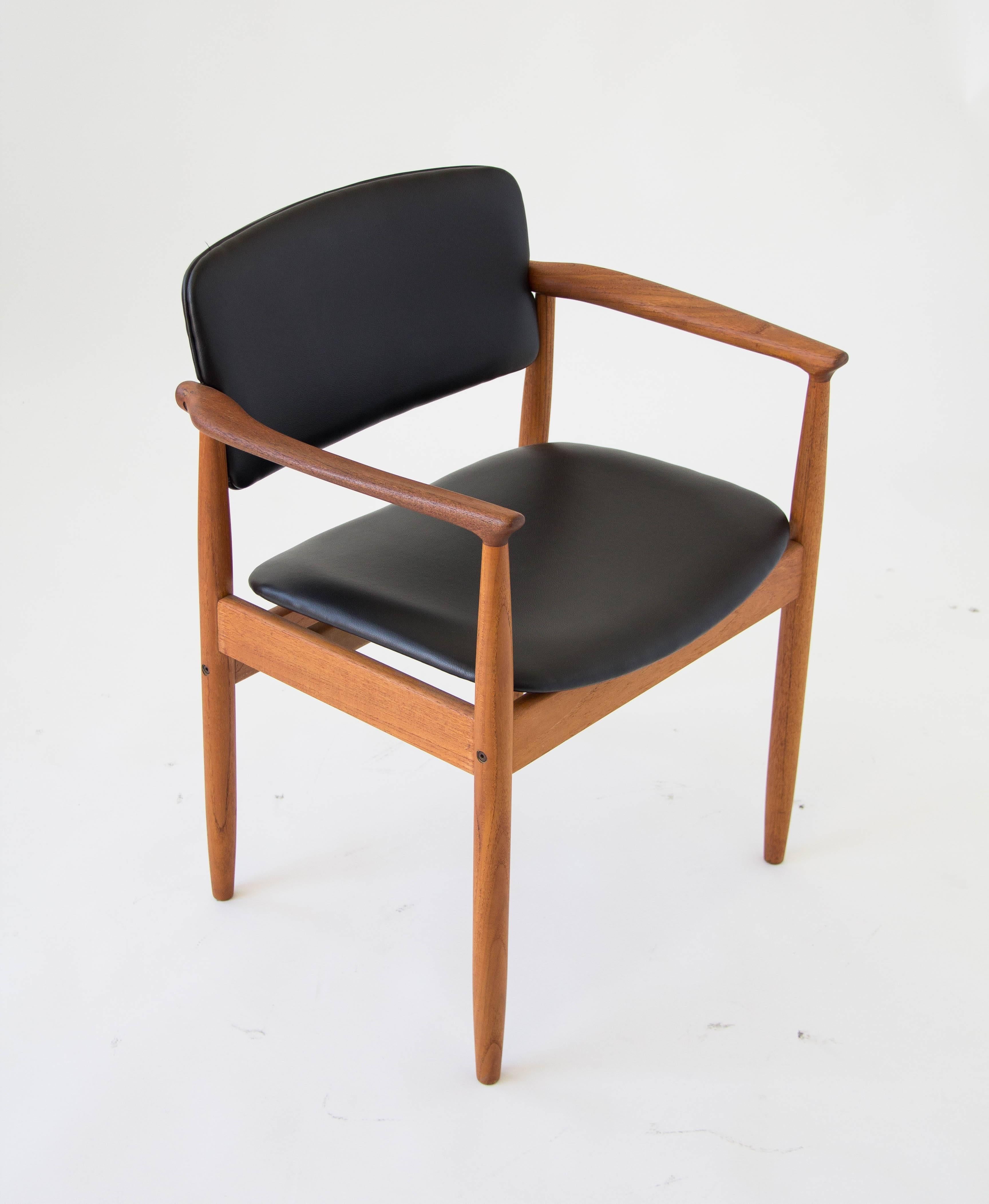 A stamped dining chair from Danish manufacturer Farsø Stolefabrik. The chair has an upholstered seat and backrest in black vinyl and a solid teak frame with curved arms and slightly tapered legs. There are two chairs still available and the listed
