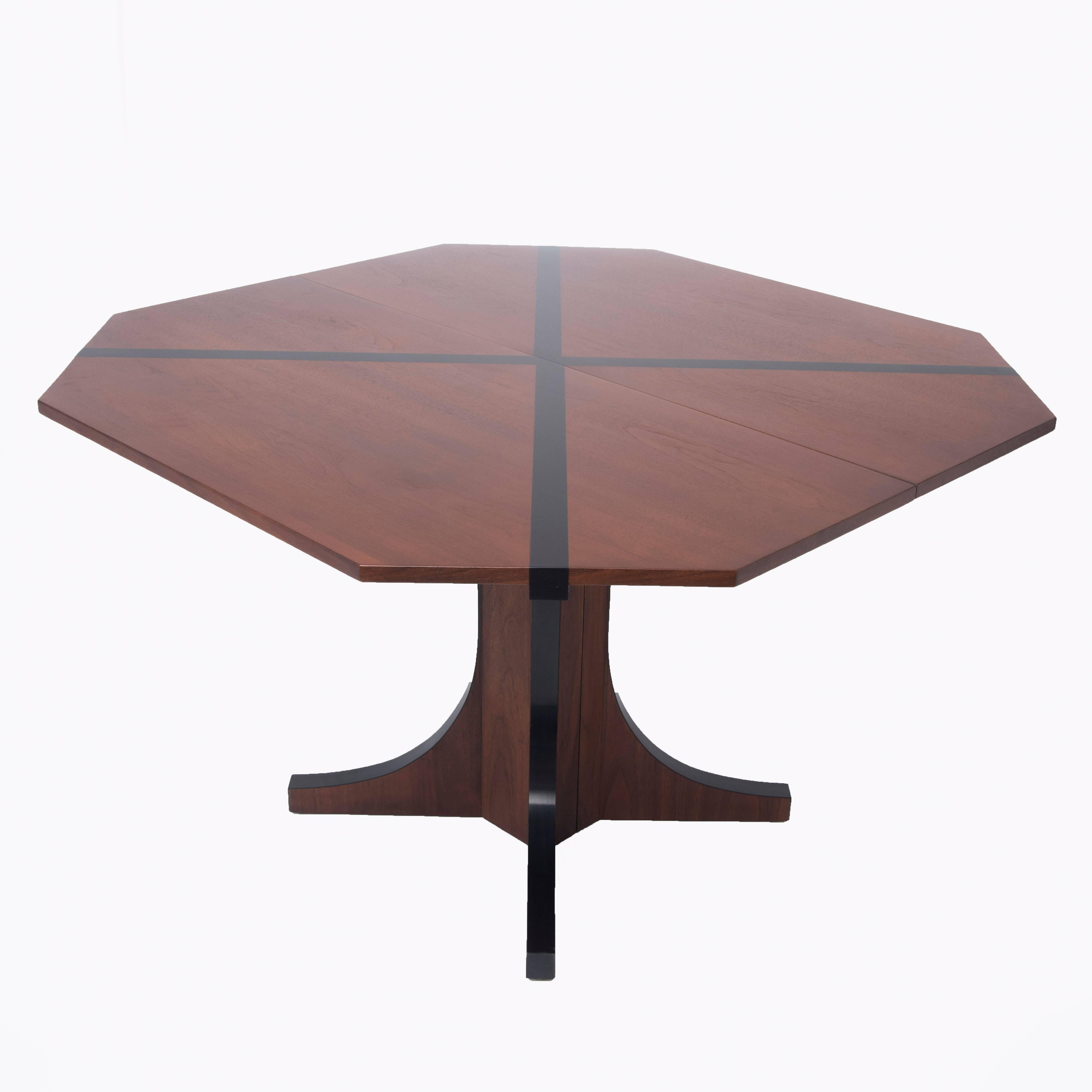 A dining table designed by John Kapel for Glenn of California with a truncated square top inlaid with a black laminate detail in the shape of an "X". The table has two walnut insert leaves that elongate the table to a rectangle with