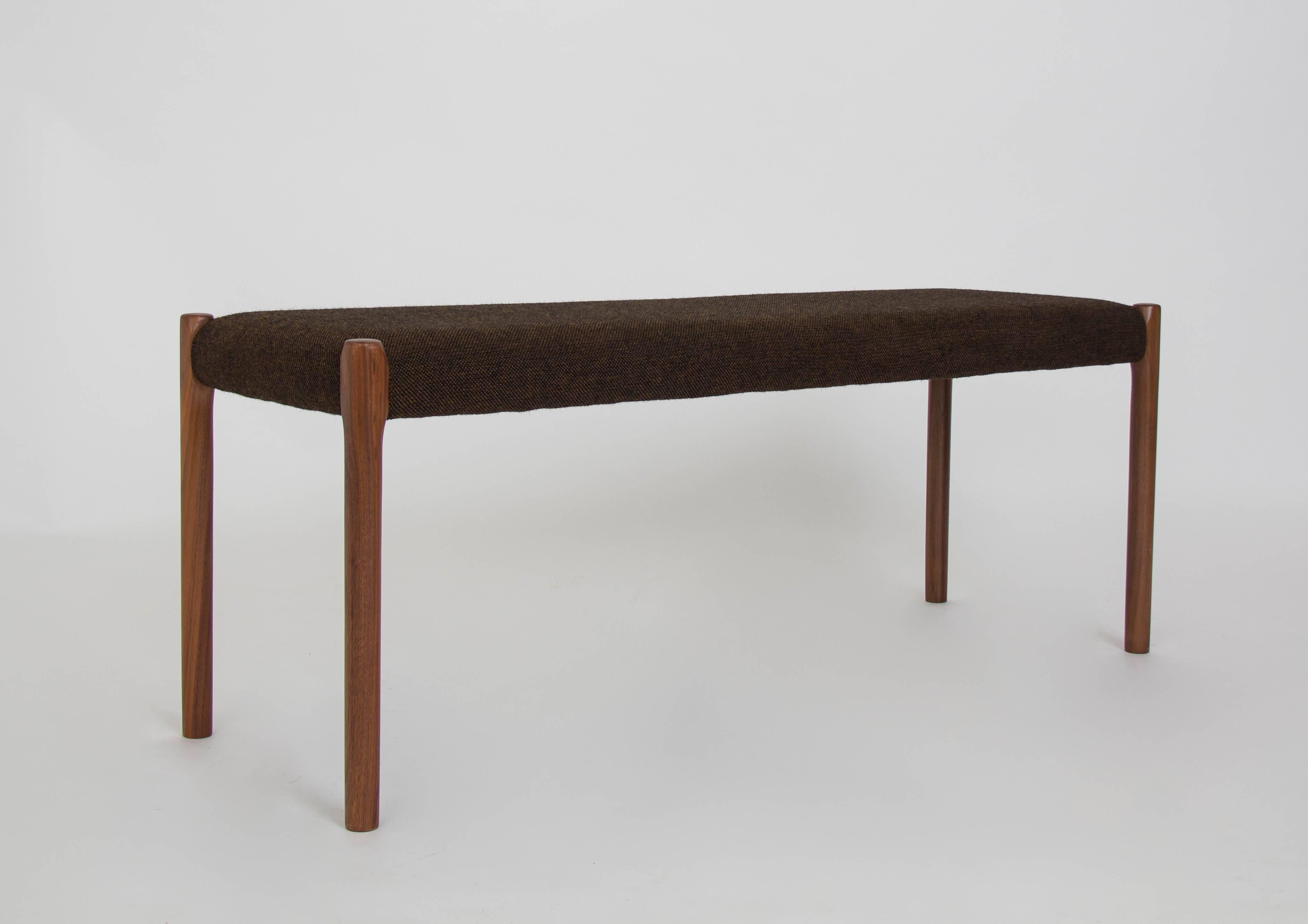 A long, upholstered bench designed by Niels Møller for JL Møller Møbelfabrik of Denmark. The model 63A bench was designed in 1963 and features tapered legs of solid walnut, and wooden frame lightly padded and wrapped in a brown wool