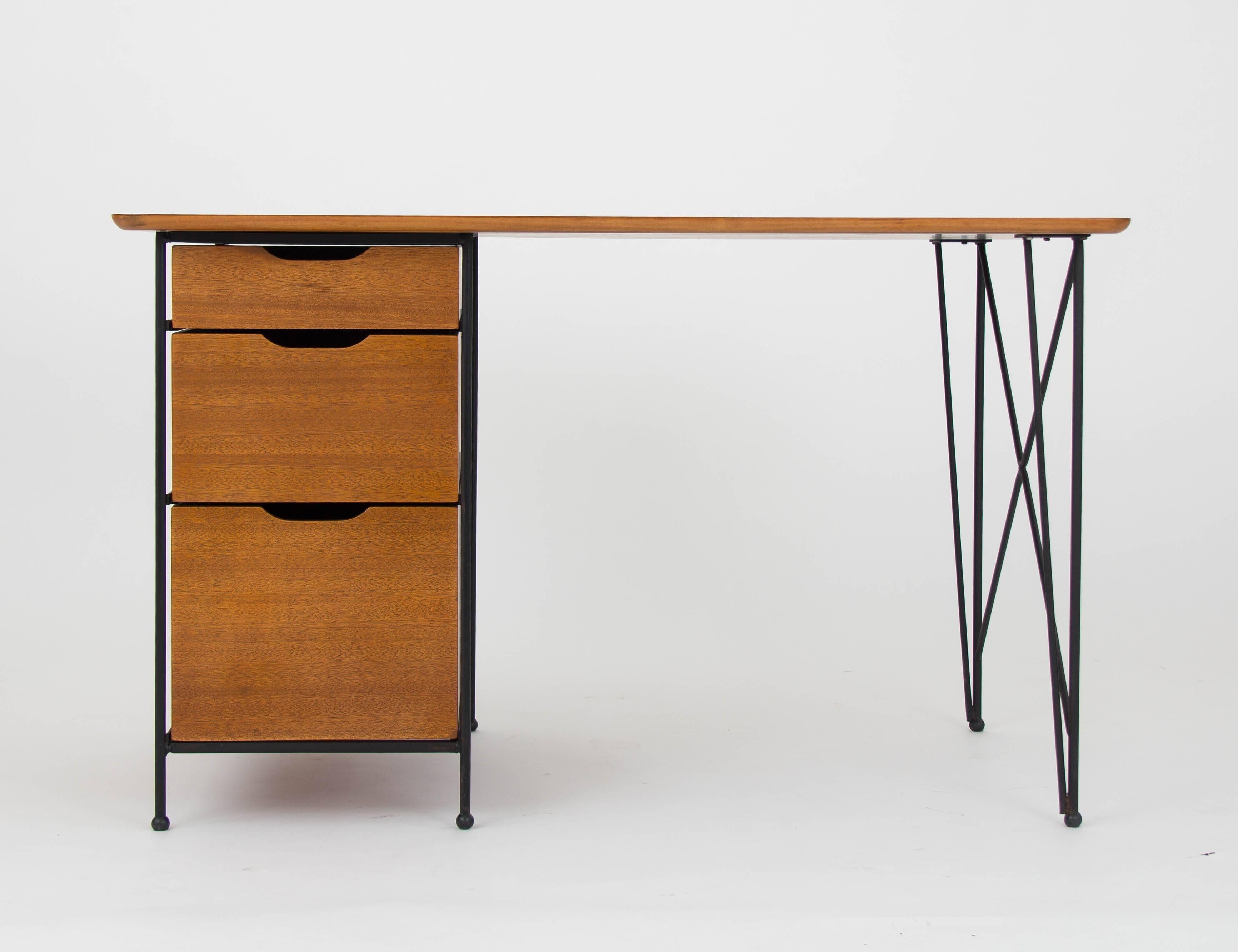 A three-drawer writing desk with minimal, modernist leanings. Produced by Vista of California, this piece has a frame of enameled steel with a work surface and drawers in mahogany wood. The left-hand drawer stack sits on exposed runners of painted