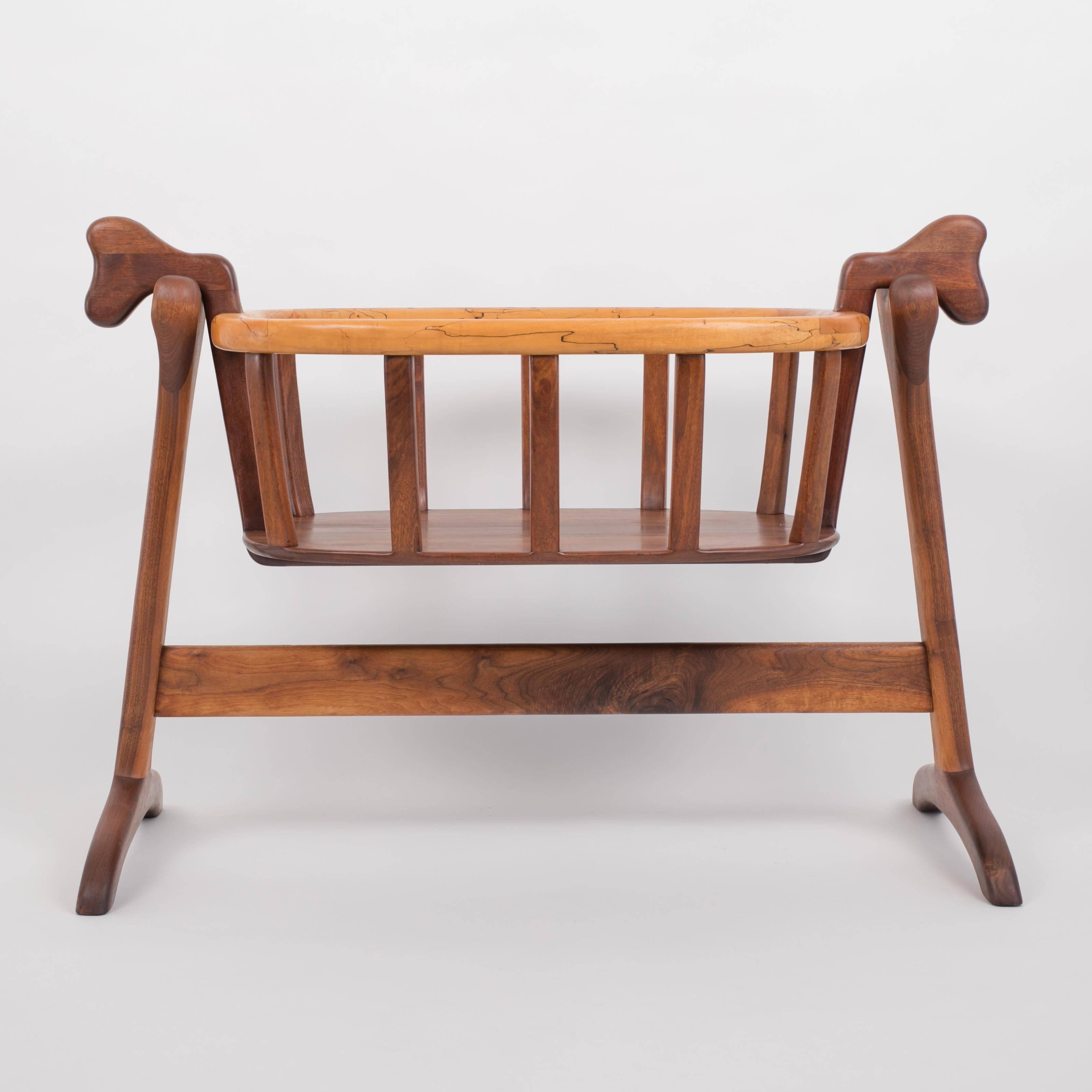 An American-made organic modern bassinet by Illinois-based craftsman Ejner Pagh. The bassinet has a wide lip in a contrasting light wood. Sculpted bars with biomorphic lines rest on the trestles of the stand and allow the piece to rock gently. A