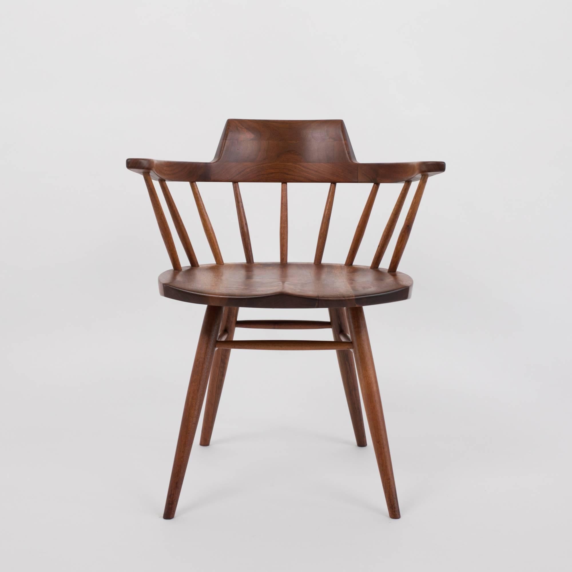 An accomplished example from American midcentury craftsman George Nakashima. The black walnut Captain chair has a curved, peaked backrest atop carved spindles. The seat is sculpted for comfort and sits on four tapered dowel legs, joined to the chair