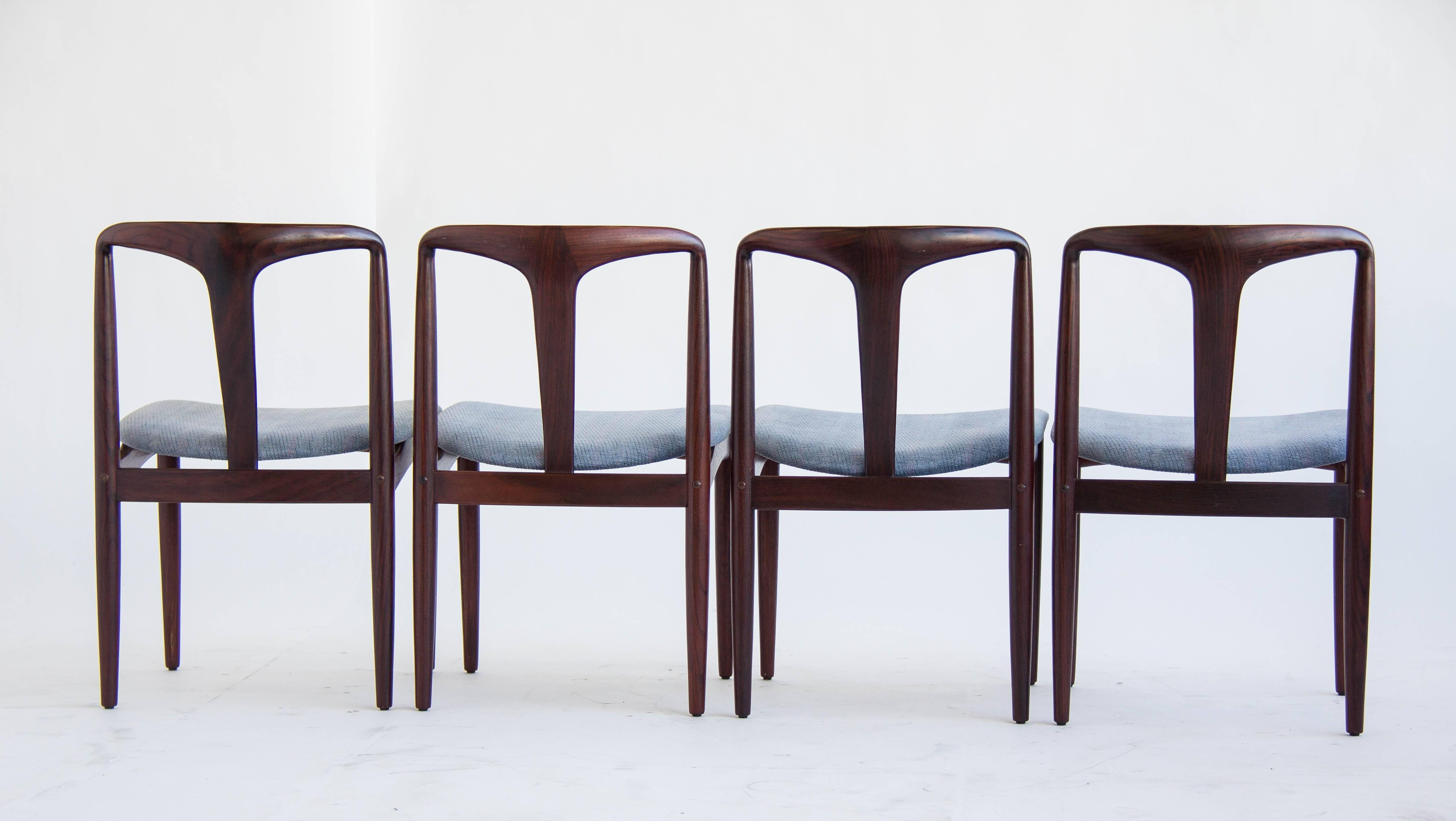 This is a set of four chairs by Danish designer, Johannes Andersen, made of carved rosewood frames and curved seat backs for the occupant's comfort. The chair's rich wood color is complemented by the original vintage blue fabric upholstery on the