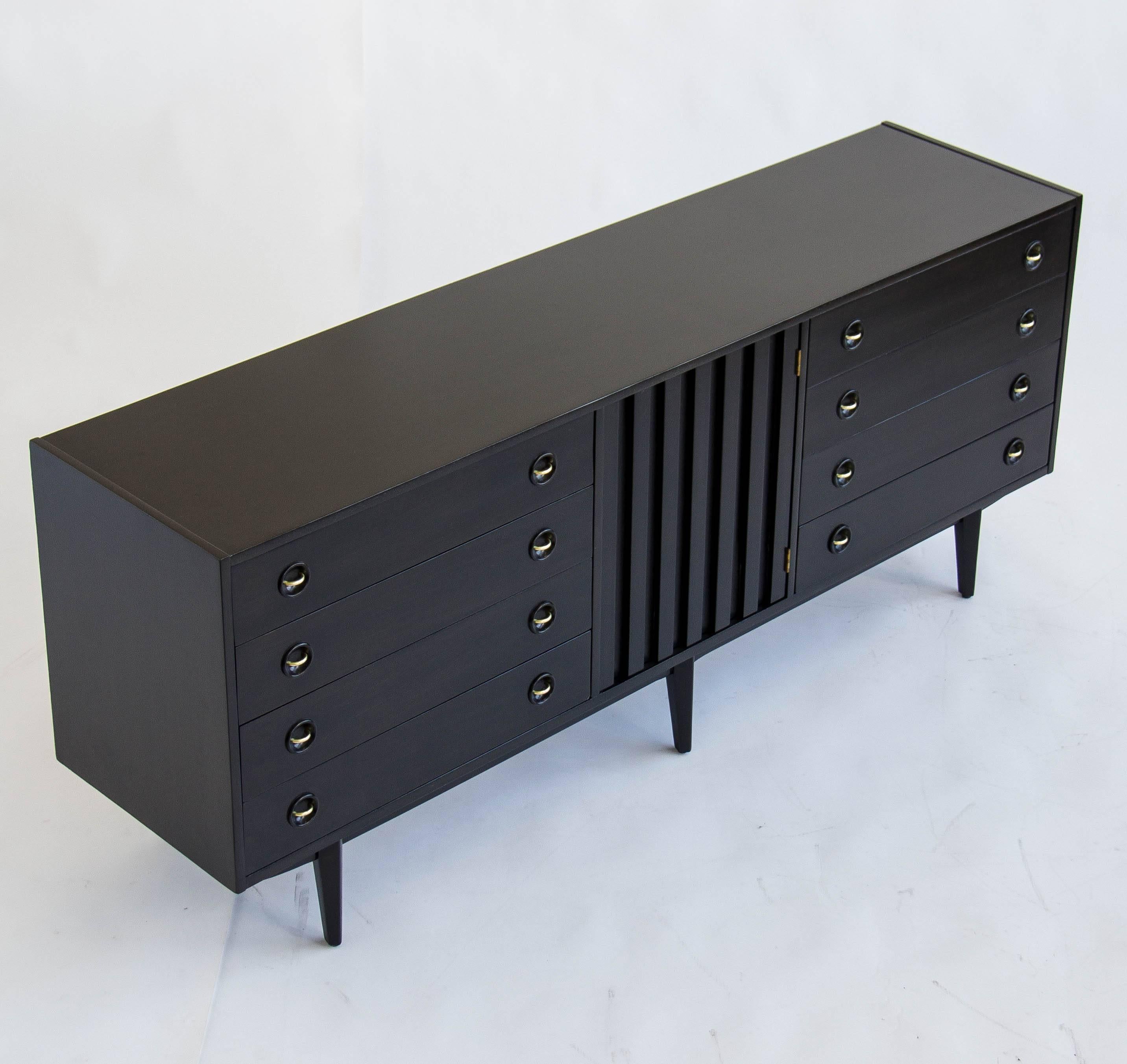 This is a fully restored and ebonized piece by American of Martinsville that can be used as a dresser or credenza. This functional piece features two sections of four drawers separated by a center section of three shelves concealed by a slatted wood