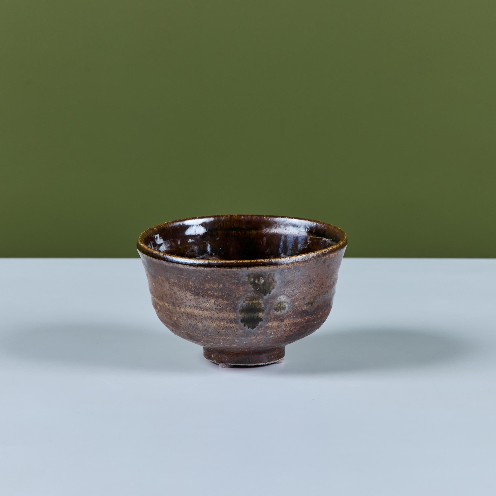 La ciotola da tè in Studio A, realizzata dalla famosa ceramista hawaiana Toshiko Takaezu e lavorata a ruota, presenta uno smalto marrone scuro e una base con piedini.

Dimensioni
6