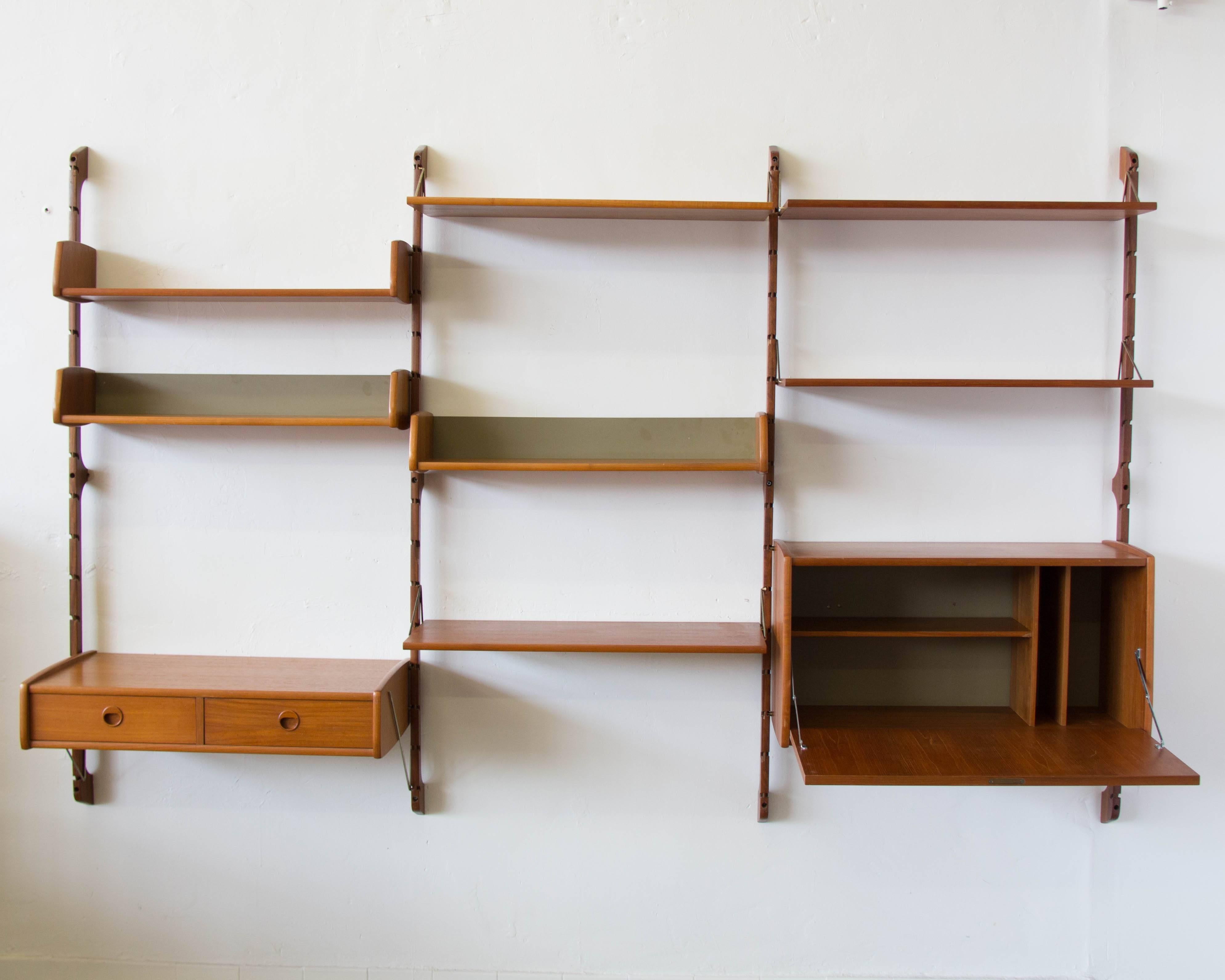 A 1960s Norwegian teak wall unit with three bays and four uprights. Left bay has a storage compartment with two drawers and two shelves above. The center bay has three shelves. The right bay has a storage compartment with a fold-down secretary style