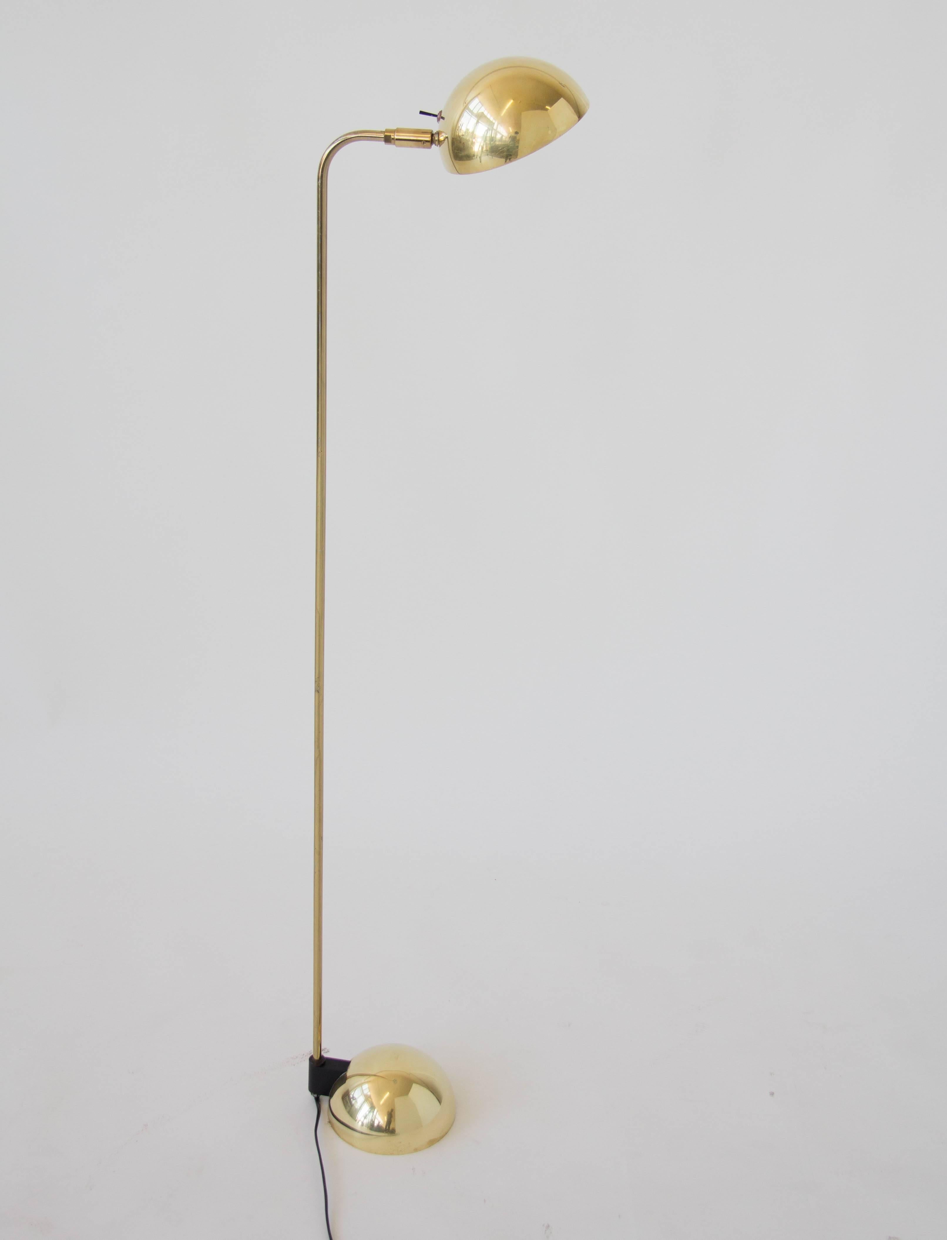A 1987 design by Robert Sonneman for George Kovacs Lighting, this brass floor lamp features a fully pivoting half-sphere shade with a halogen bulb. A slightly curved arm of brass joins the shade to a similarly shaped base that contains the