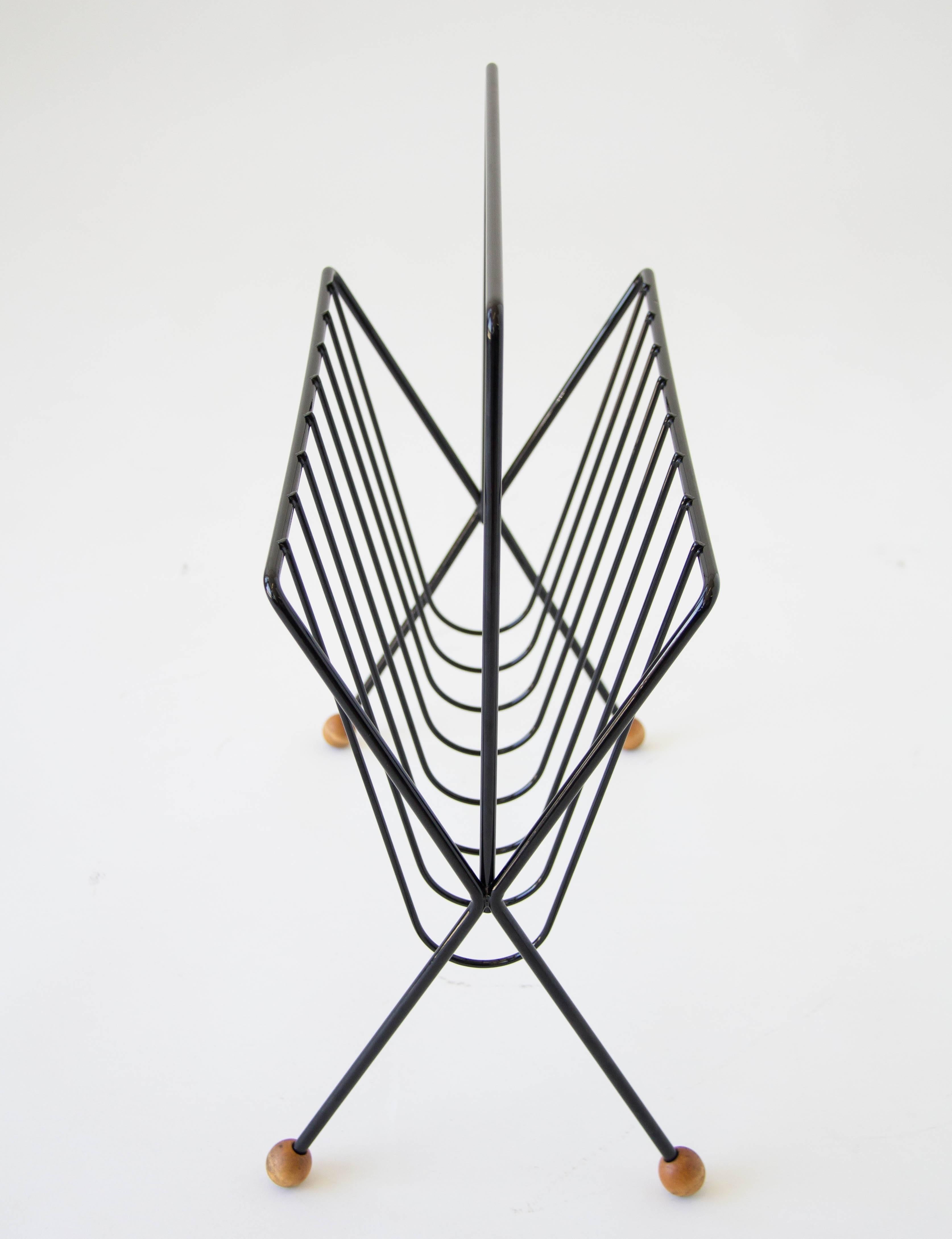 American made wire magazine rack by New York designer Tony Paul. The rack has a skeletal frame with bent spokes to hold your items and crossed legs finished with wooden ball glides. The piece has been powder-coated for a glossy black