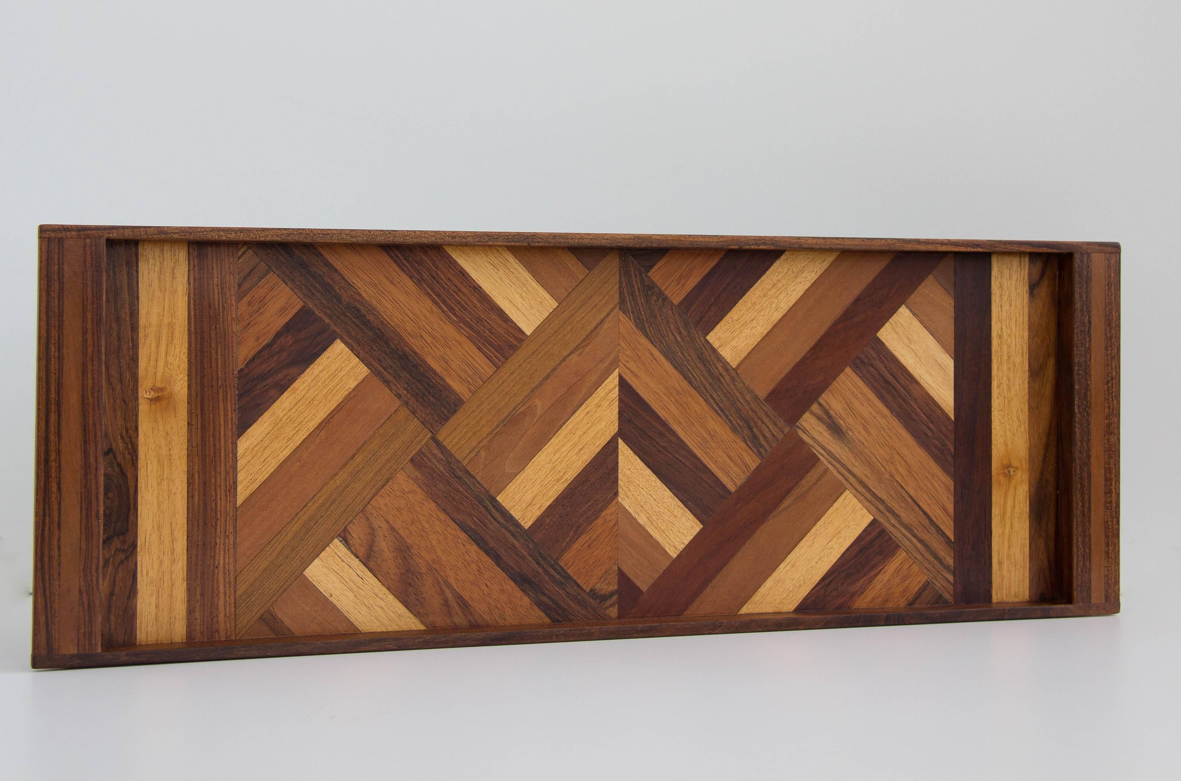 A narrow serving tray by Don Shoemaker for Senal of Mexico. The tray has a dark tropical wood frame with integrated handles at either end, and the tray surface is inlaid with precious woods in a geometric pattern. 

Condition: The tray has been