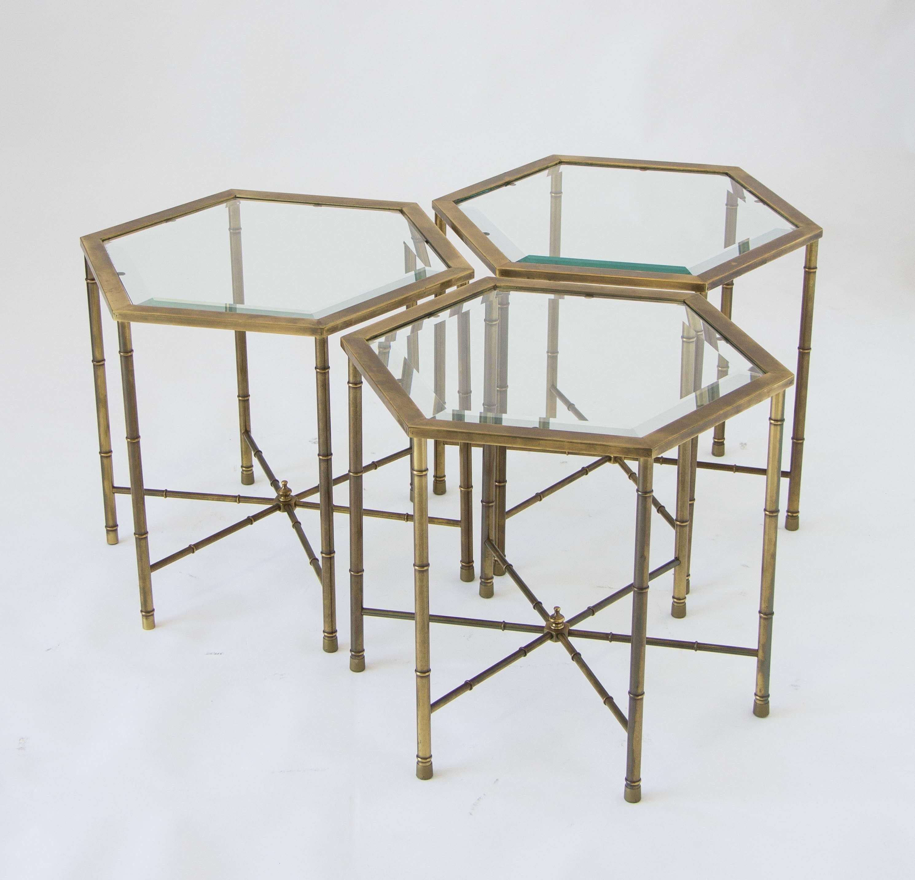 Three hexagonal brass side tables from Grand Rapids manufacturer Mastercraft. Each table has a six-sided frame in burnished brass, with ribbed legs and six brass spoke cross-supports. Removable table tops are the original beveled glass. The tables