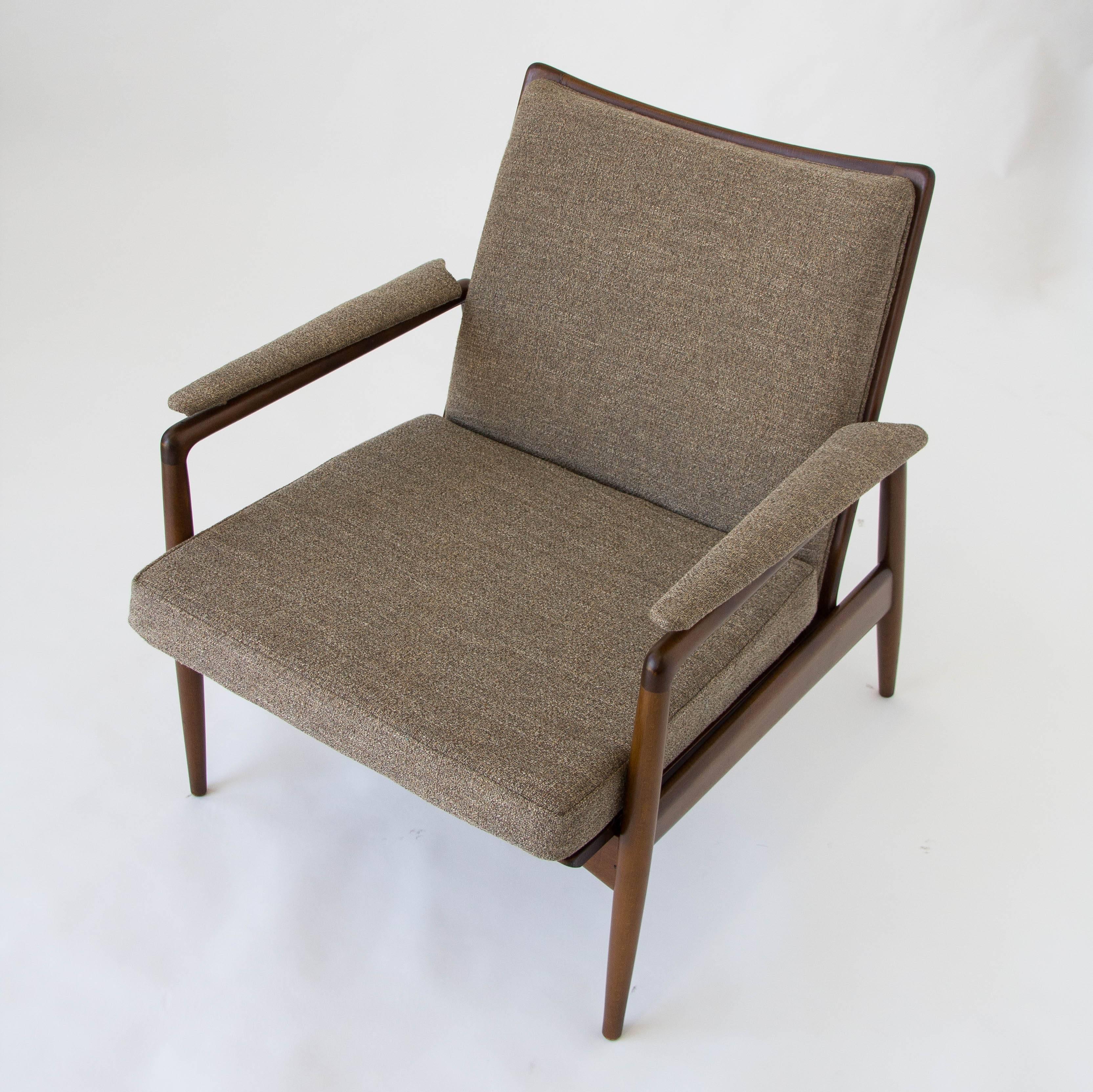 A single Selig lounge chair has a dark frame of stained beech and dove grey bouclé upholstery. The open back of the chair show the integrated backrest from either side. The matching upholstered armrests appear to float over the chair frame. The red