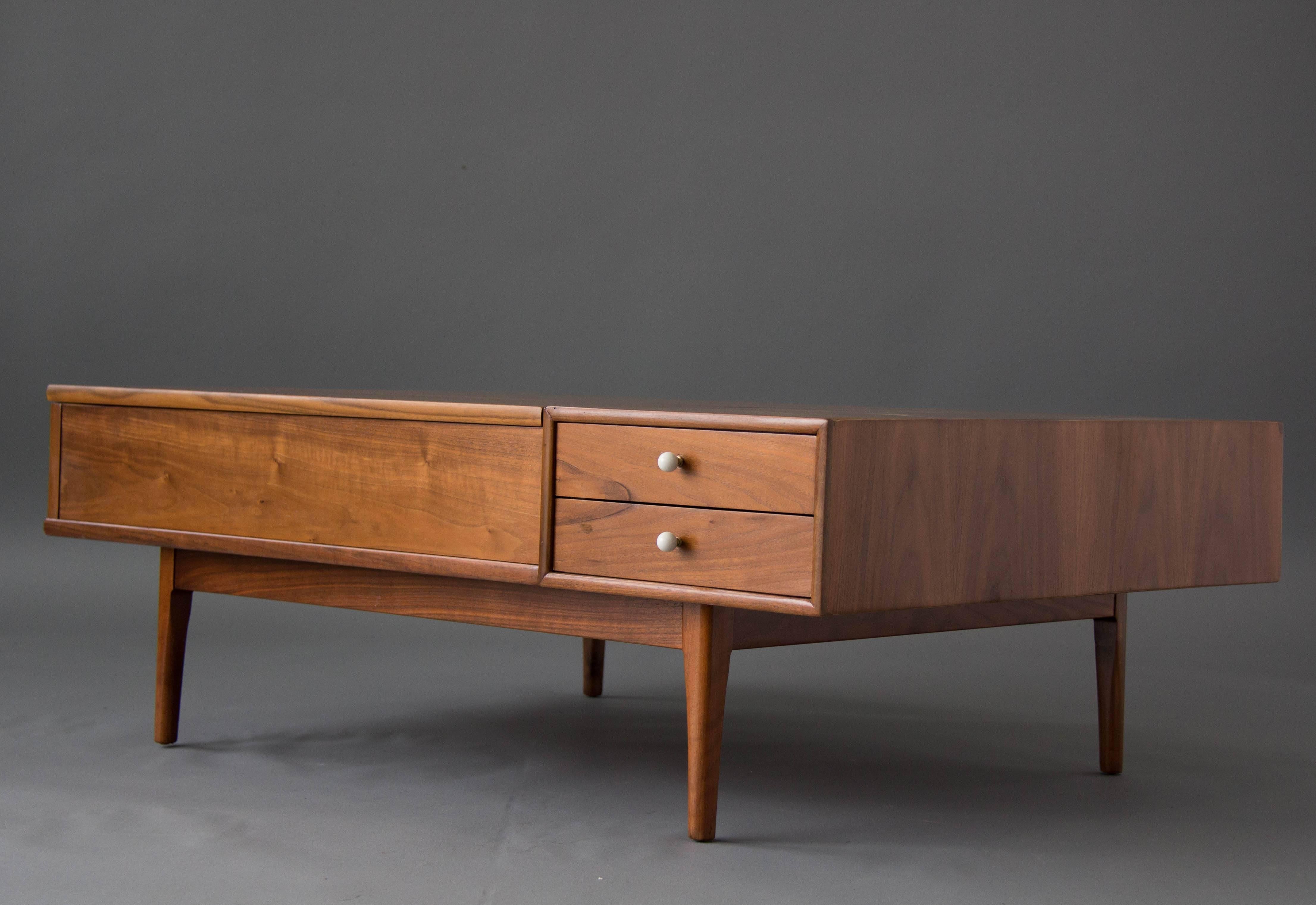 From the iconic Drexel Declaration collection by Kipp Stewart and Stewart MacDougall, this is a deep, rectangular table in walnut wood on recessed legs. Two drawers with signature porcelain drawer pulls sit in the right front corner, and a panel