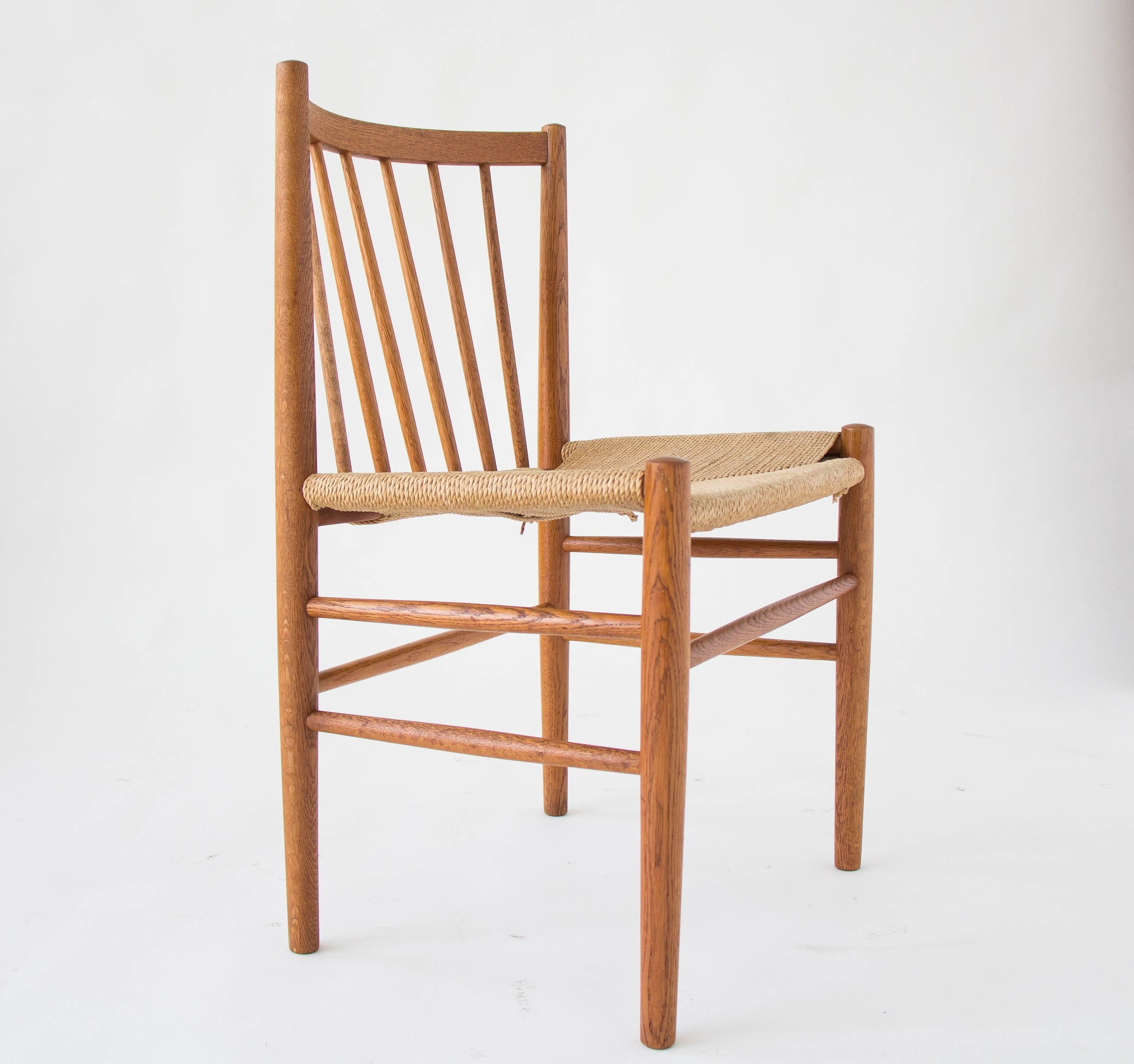 A set of six oak modeled after the J80 dining chair from FDB Møbler, designed by Jørgen Bækmark. Each chair has a curved backrest and six vertical dowels pitched at an angle for support and comfort. The comparatively wide seat is woven in paper