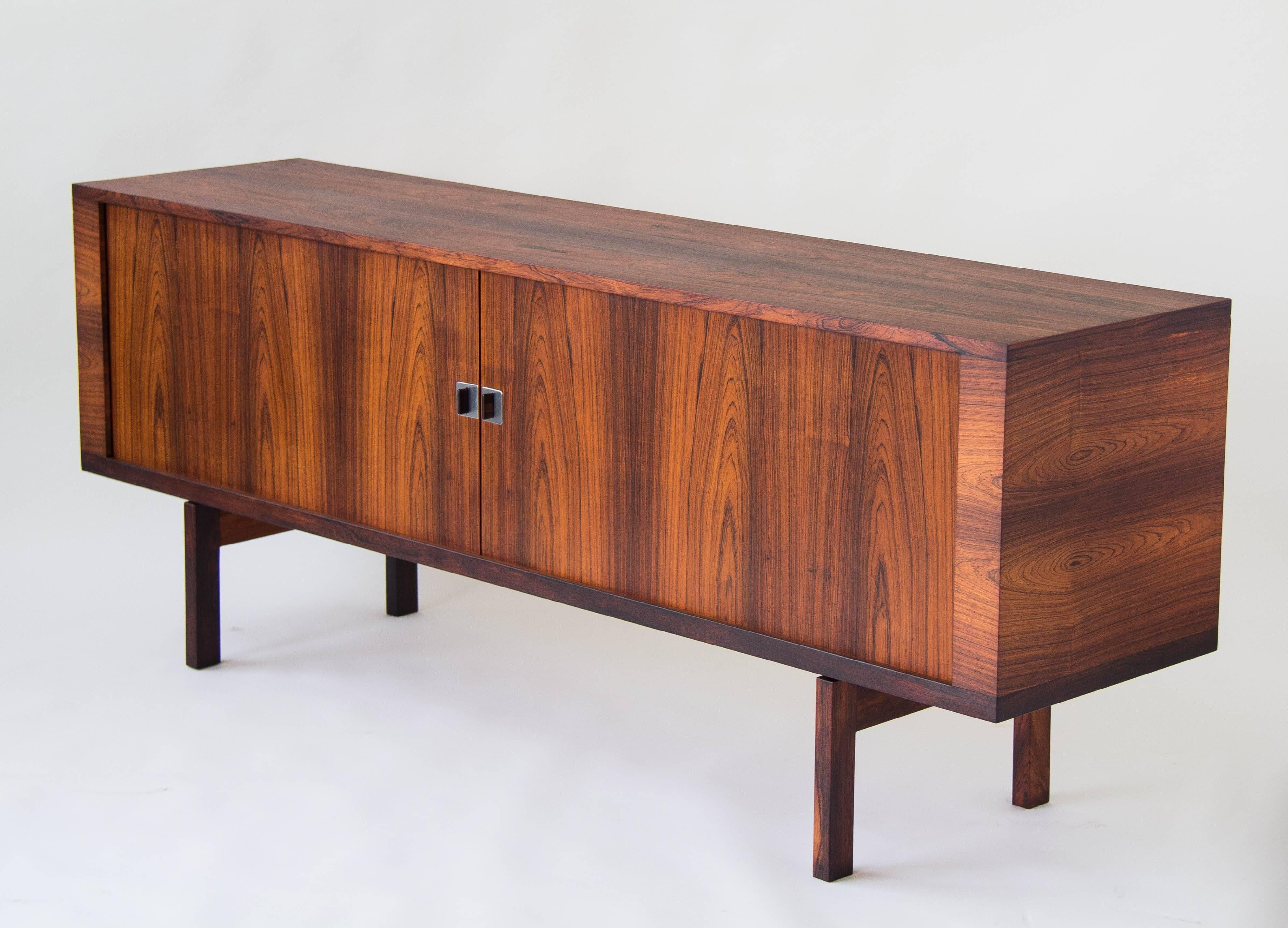 A rosewood credenza with stunning grain, designed by Hans J. Wegner for Ry Mobler. The piece has tambour doors with rosewood pulls mounted on square plates of polished steel. The interior is finished entirely in soaped oak, with each outer