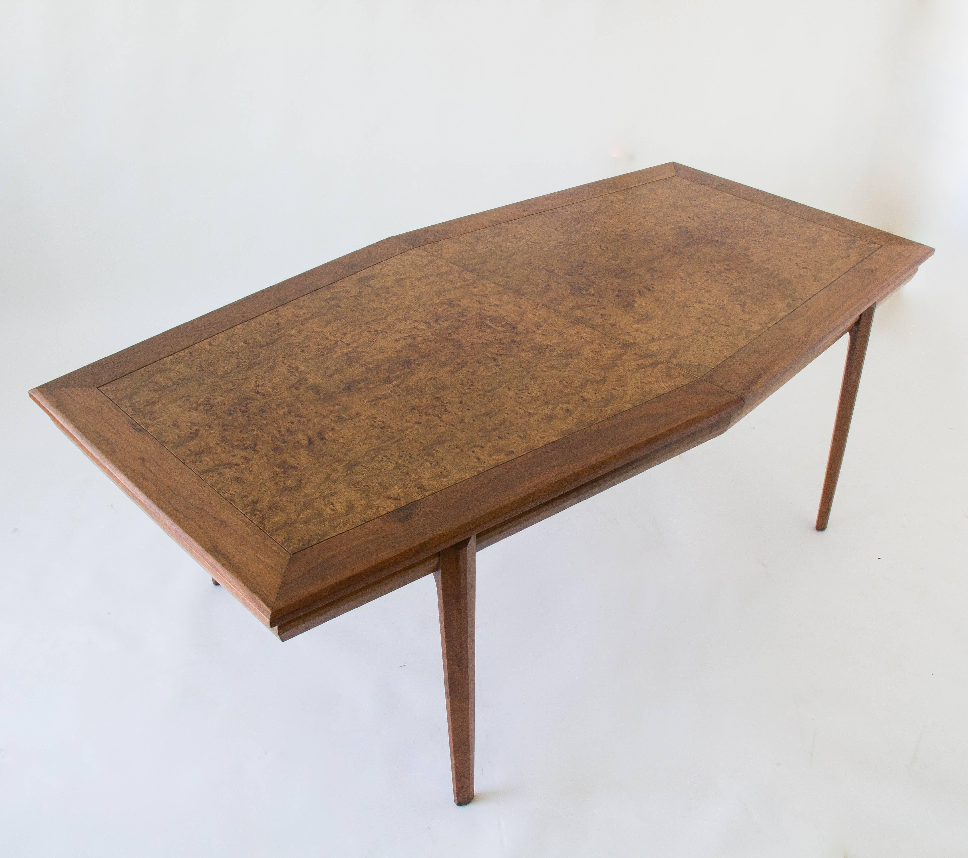 An elongated hexagonal dining or conference table, designed by Maurice Bailey and produced by Cal-Mode of Culver City (know subsequently as Monteverdi Young. The tabletop has inlaid burlwood in a corresponding hexagonal shape. Two extending leaves