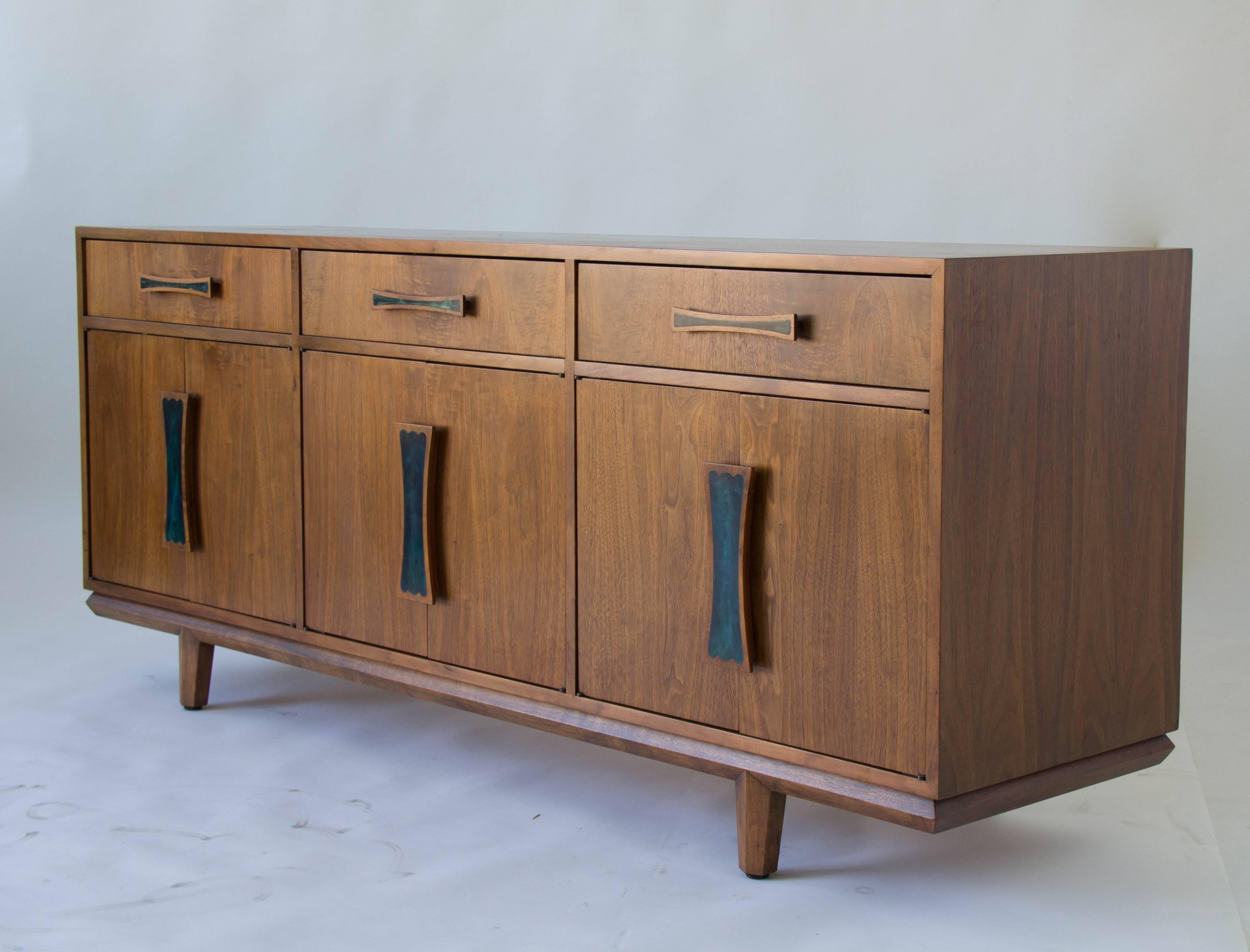 A credenza or sideboard with plenty of storage. This piece by Cal-Mode (subsequently renamed Monteverdi Young) has a walnut case. Each drawer and door is fitted with a sculpted wood handle, inlaid with teal blue resin. Each storage cupboard has an
