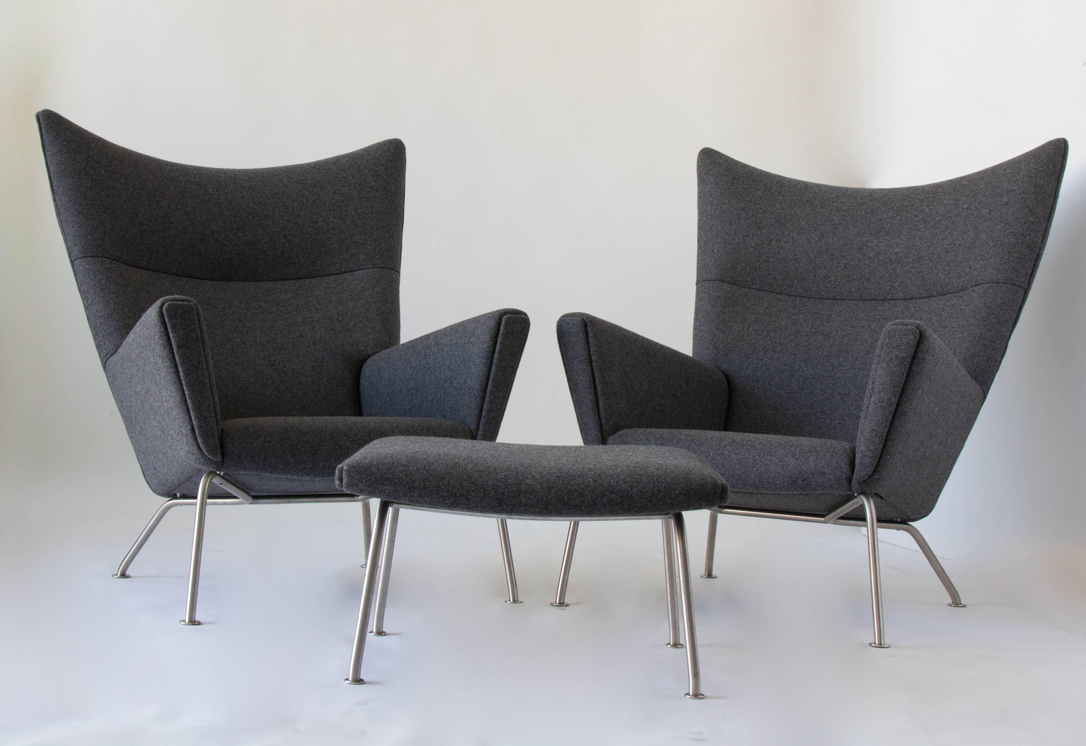 A pair of CH446 wingback chairs and with matching CH446 ottomans designed by Hans Wegner in 1960 and produced by Carl Hansen & Søn. The set has solid birch frames upholstered in a rich Maharam wool. Each piece sits on a base of brushed steel