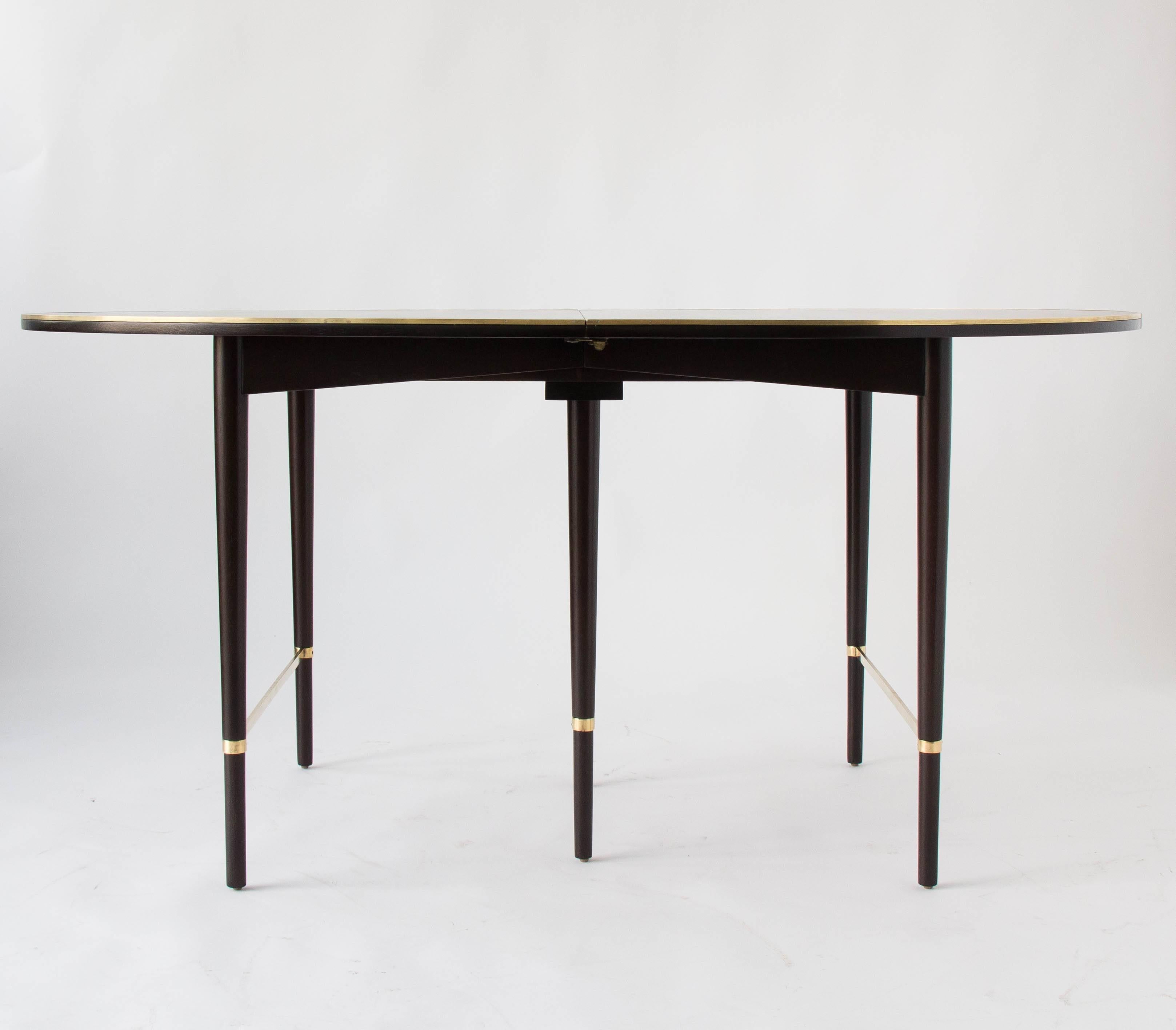 An oblong dining table from the Connoisseur line, designed by Paul McCobb for H. Sacks & Sons. Constructed from ebonized mahogany, the table has rounded edges and recessed, tapered legs with polished brass stretchers. It’s length is highly