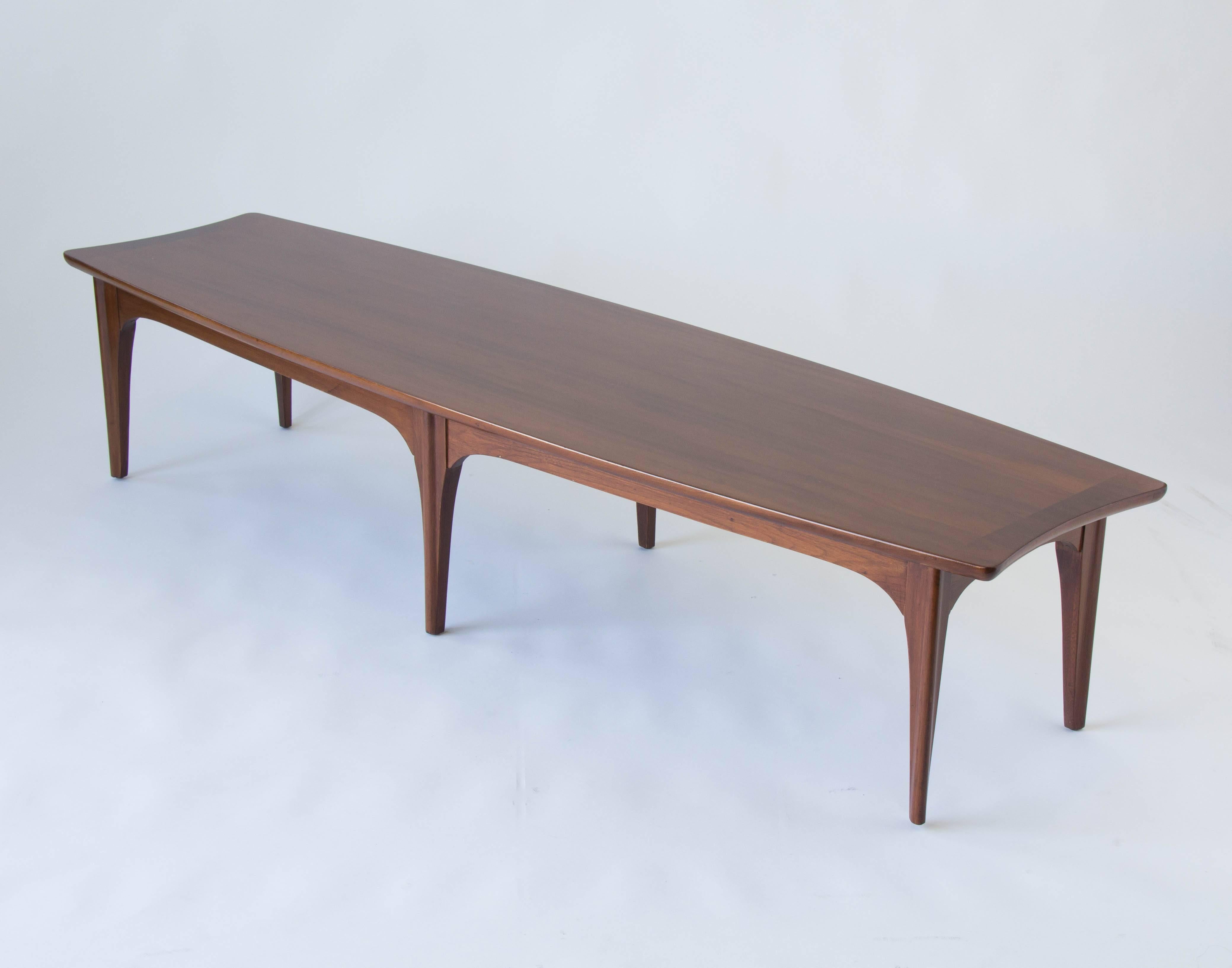 A long surfboard coffee table from the Kent Coffey 'Perspecta' line has six legs made in the U.S., circa 1960s. The traditional surfboard shape has been manipulated in incorporate peaked end pieces, inlaid with rosewood accents. 

Condition: Table