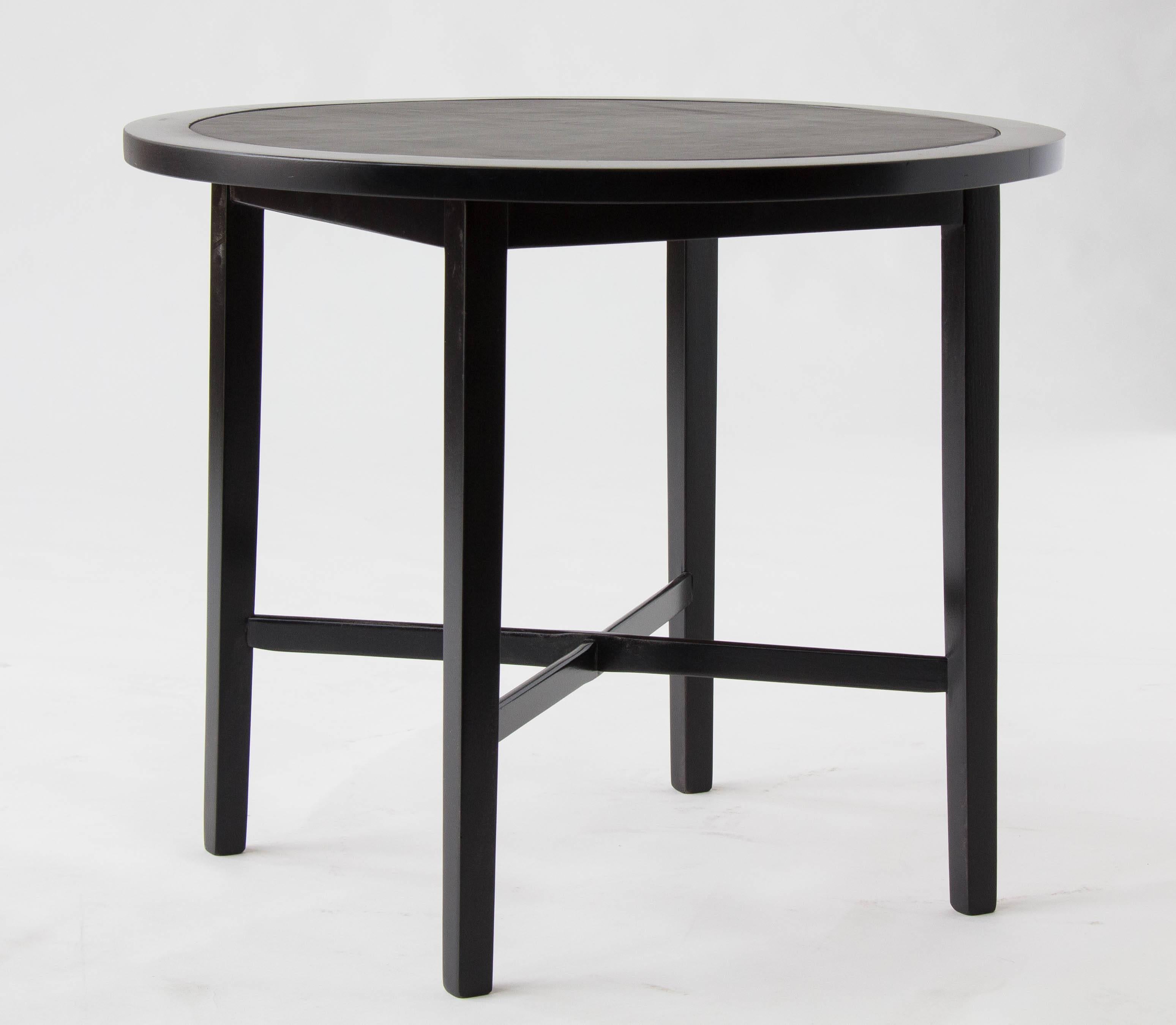 A round side table from the perimeter group, designed by Paul McCobb for Winchendon Furniture in 1959. The table has an ebonized frame around a leather covered tabletop. The delicate frame has four legs with cross supports in an X formation. The