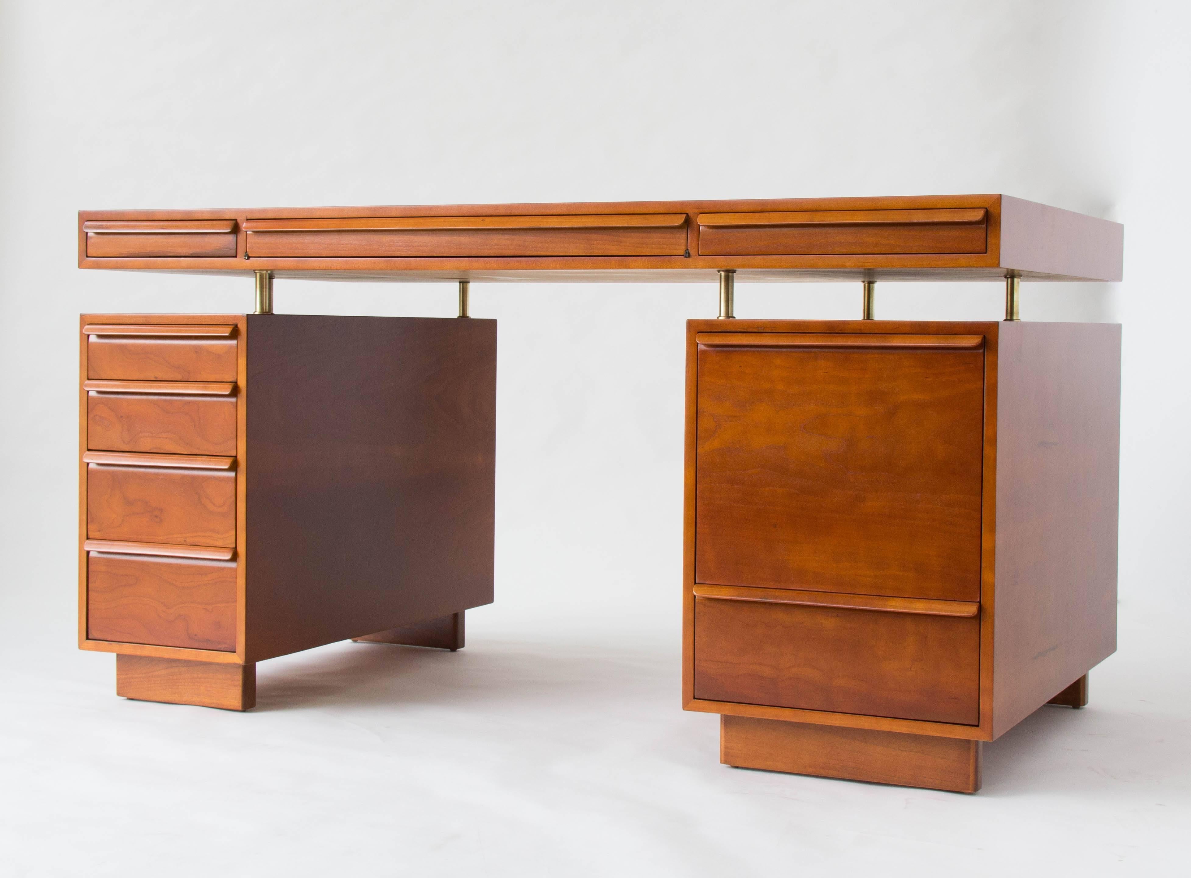 An executive desk in warm-toned cherrywood with a floating workspace on brass spacers. The two drawer stacks are mirrored on either side of the desk, which is configured for two workers. There is a shallow pass-through compartment at the center of