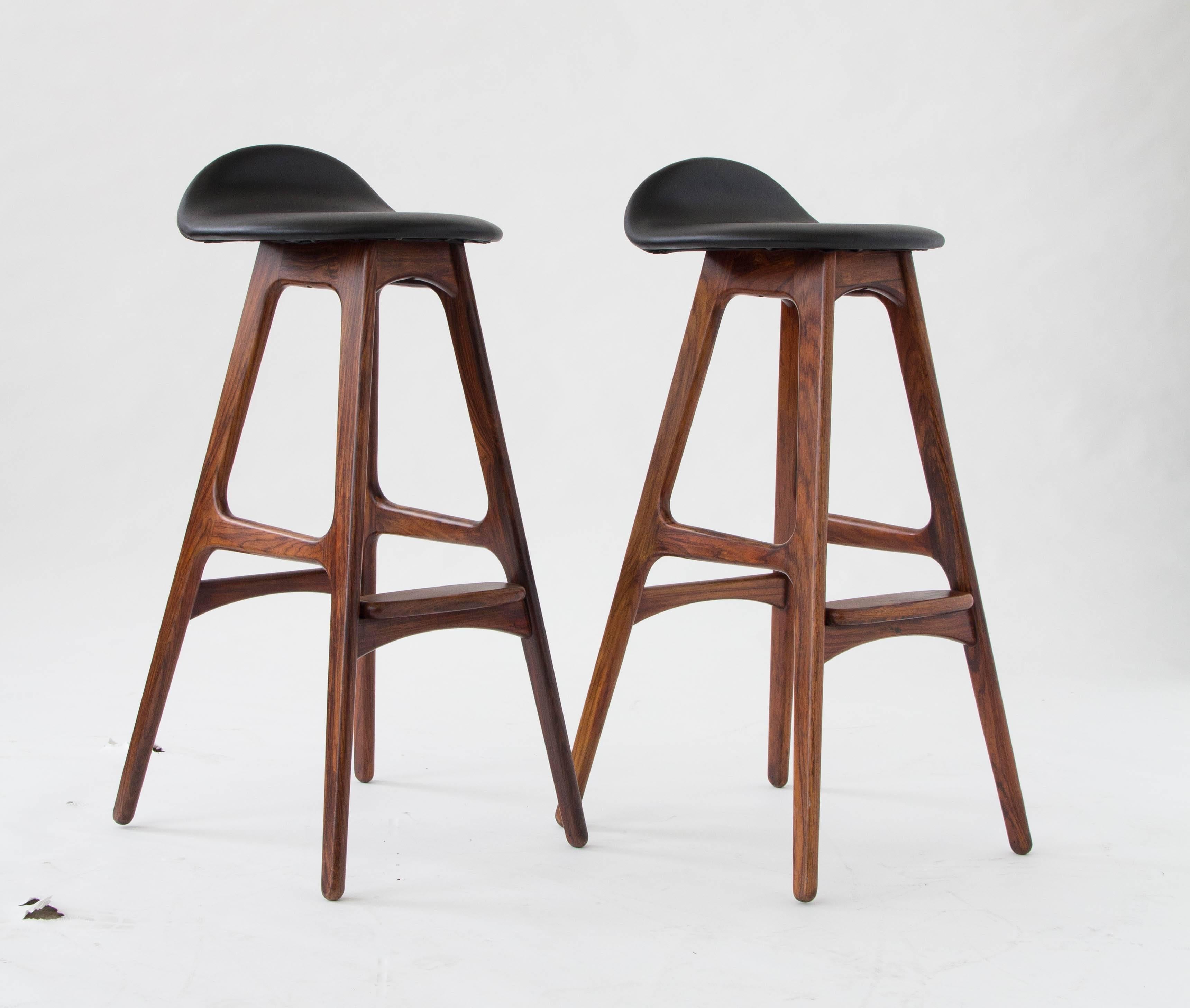 A pair of bar stools with rosewood frames designed by Erik Buch and produced by O.D. Møbler of Denmark. The frames are sculpted with slightly rounded angles and a paddle-shaped footrest in matching rosewood tops the front support. The seats are