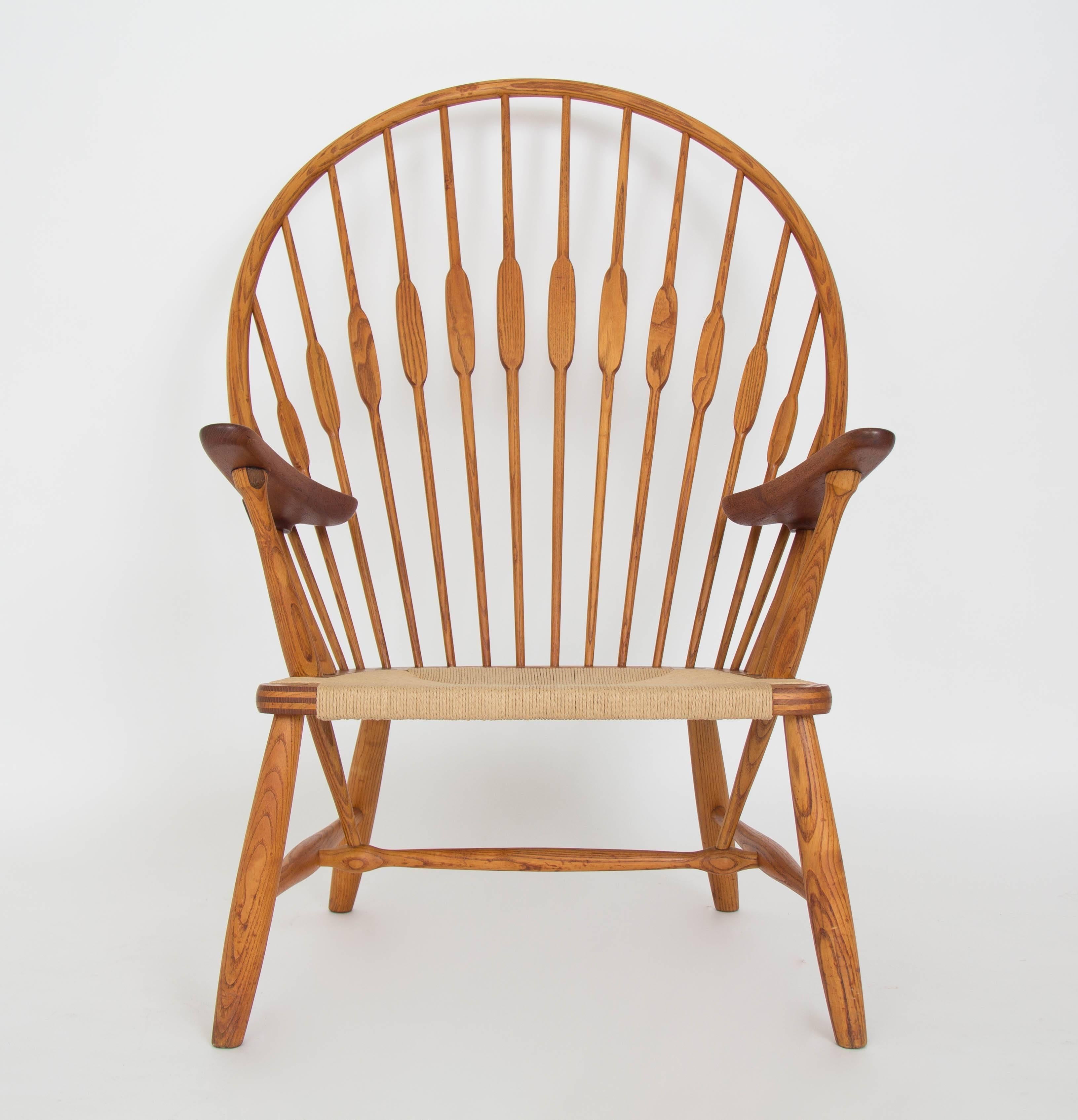 Designed in 1947, this fully restored Hans Wegner peacock chair features windsor chair styling and characteristic attention to detail. The solid wood frame has a high, arched back strung with round wooden supports that flatten where the chair meets