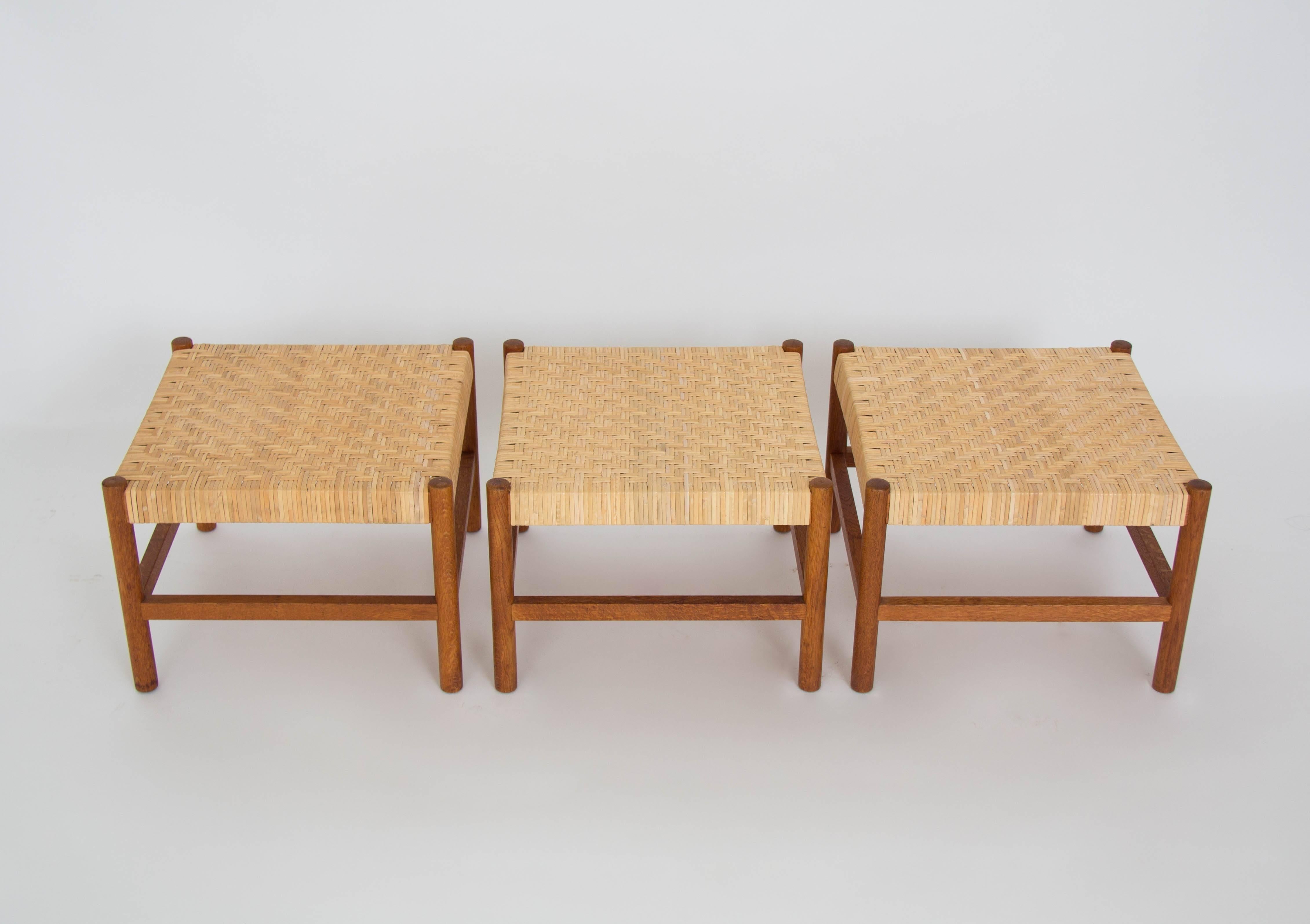 Three low, square stools designed by Axel Thygesen and produced by Interna of Denmark. The frame is constructed of a patinated oakwood and the seat is made of woven cane. The square design is supported by dowel legs of solid oak set at each corner