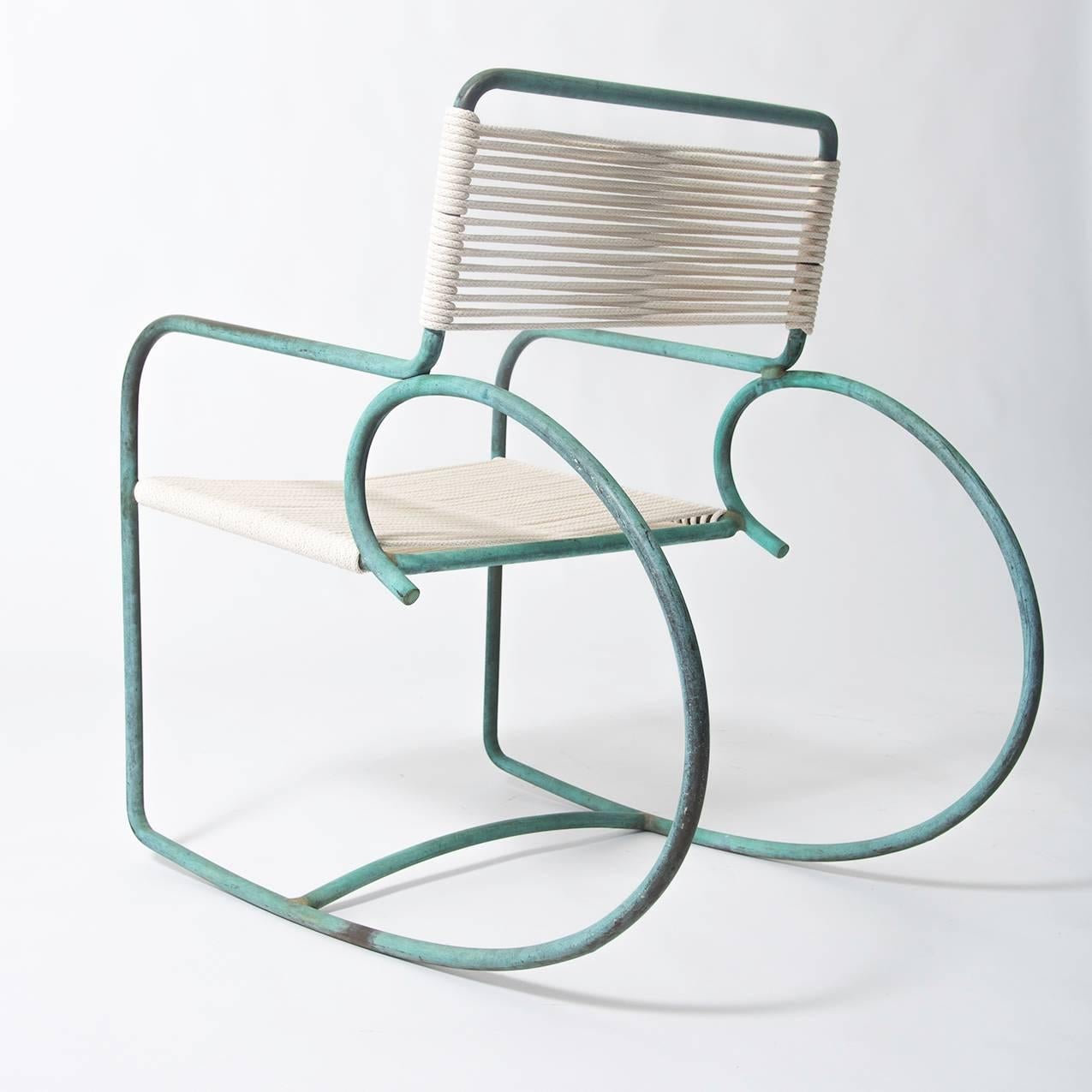 Walter Lamb's patio rocking chair, produced by Brown Jordan. The chair has a sculptural shape, with a single formation of tubular bronze forming the backrest, arms, and exaggerated round runners. The back and seat are strung with cotton rope,