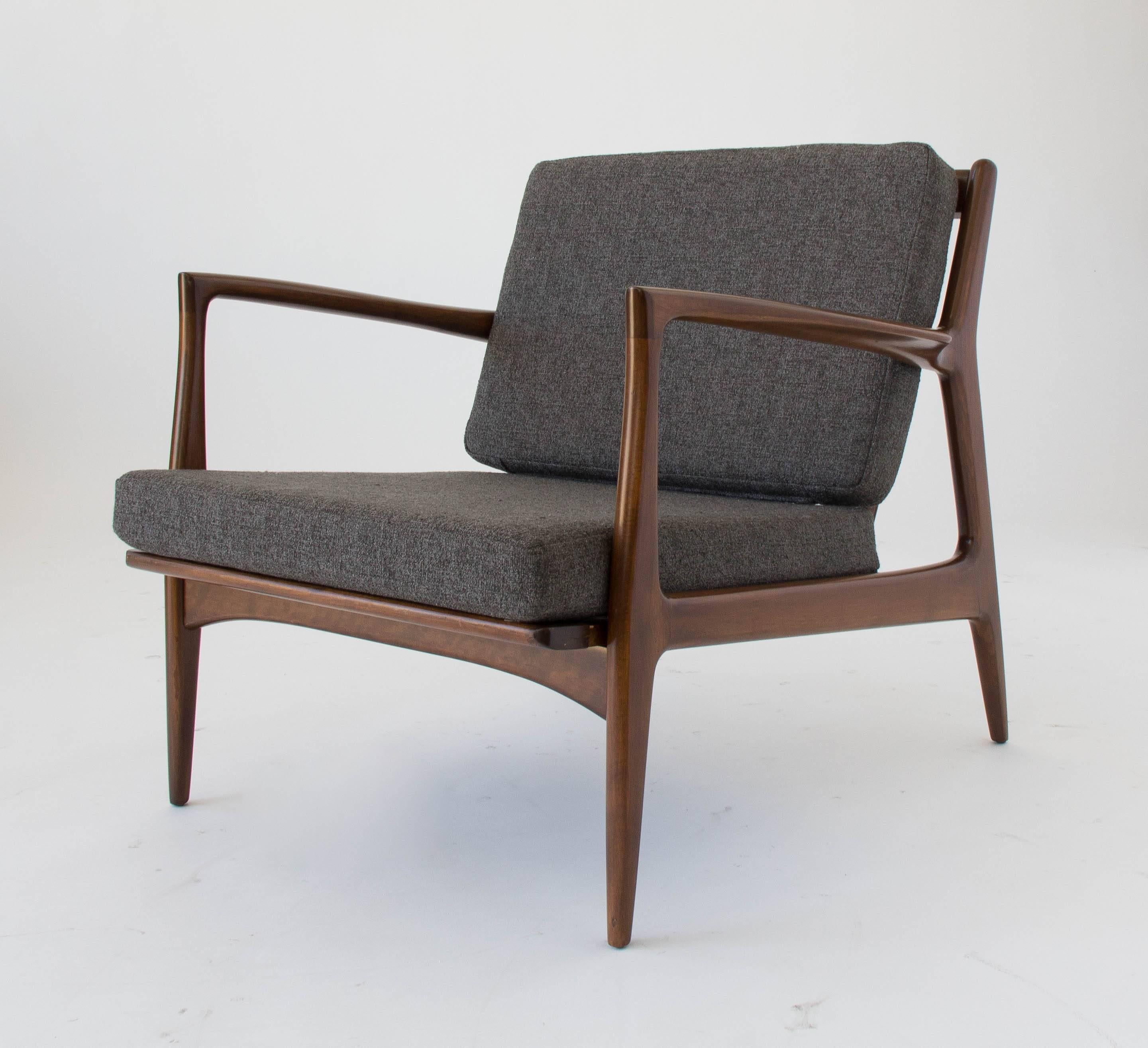 Danish Modern lounge chair in walnut-stained beech designed by Ib Kofod-Larsen for Selig. The chair has slightly curved armrests and a angled frame. The charcoal grey bouclé cushions are supported at by an open-back frame with sculptural spokes. The