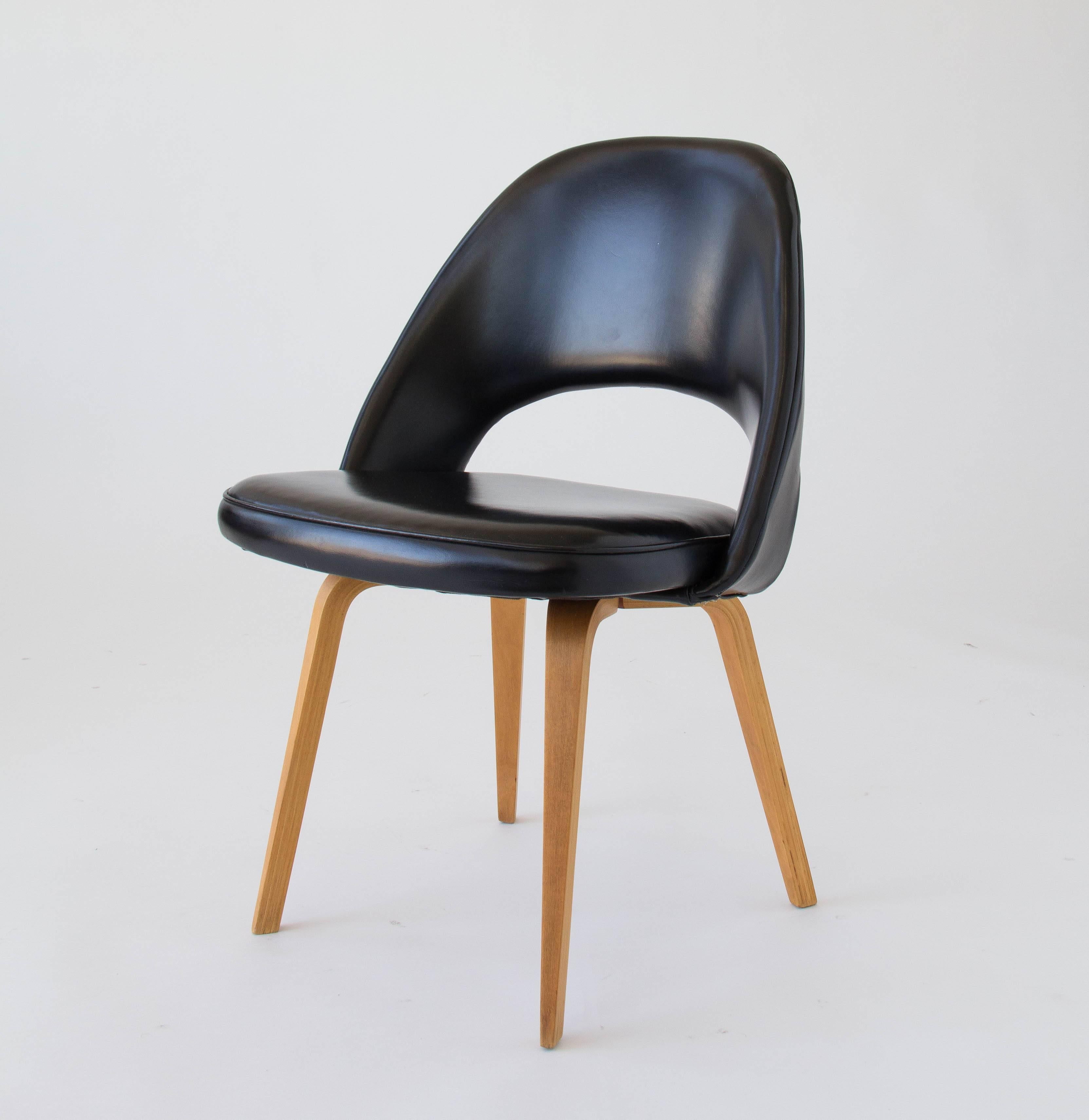 An iconic design from 1950 by Eero Saarinen for Knoll. This example is the armless version with wooden legs. Suitable for use at home or in the office, the chair has a curved backrest and rounded seat cushion upholstered in the original black vinyl