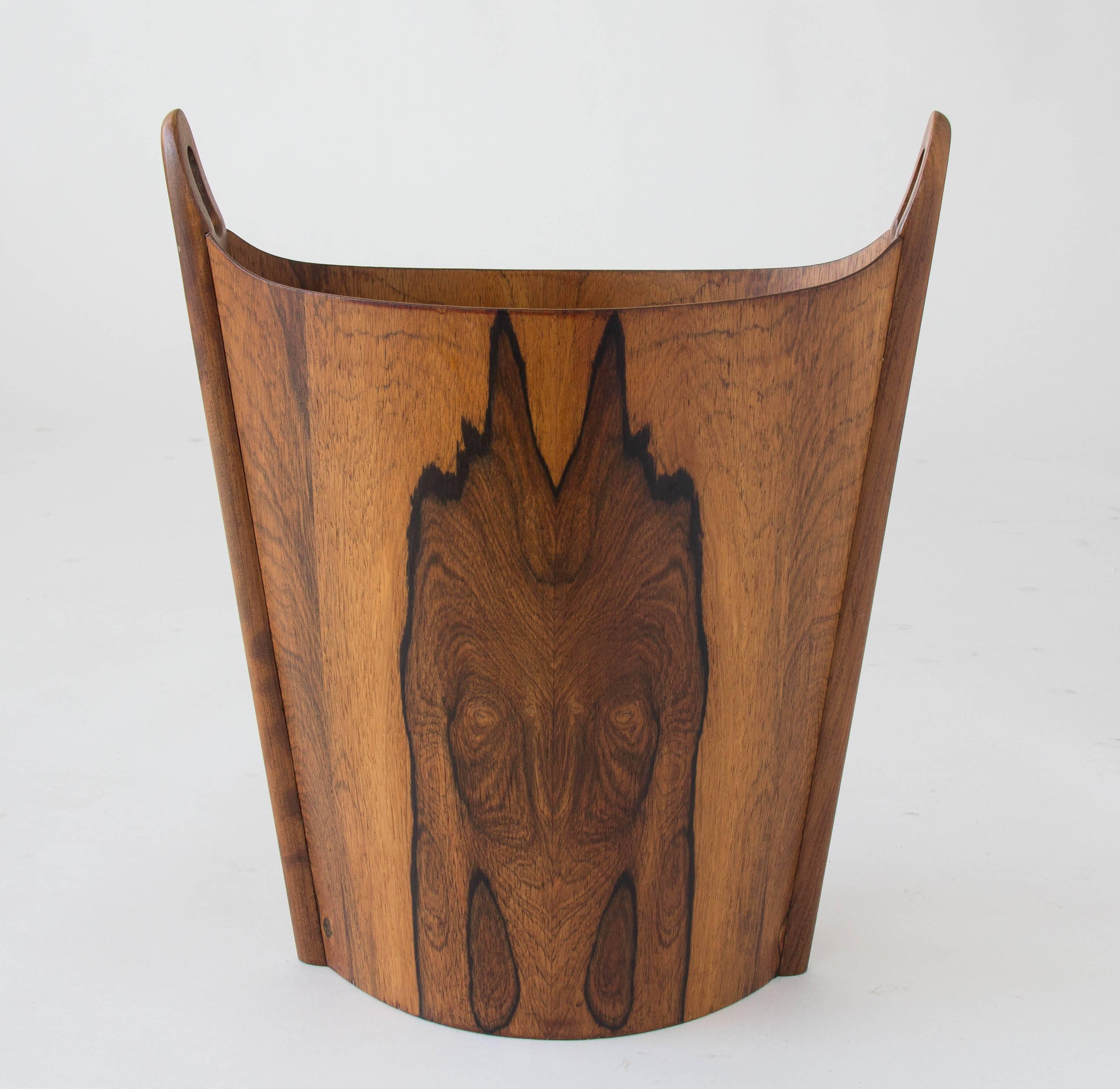 A wastebasket with delicate construction in highly figured rosewood, designed and produced in Norway by Einar Barnes for P.S. Heggen. The oblong vessel has a ridge at either end of solid rosewood with a round, integrated handle. 

Condition: